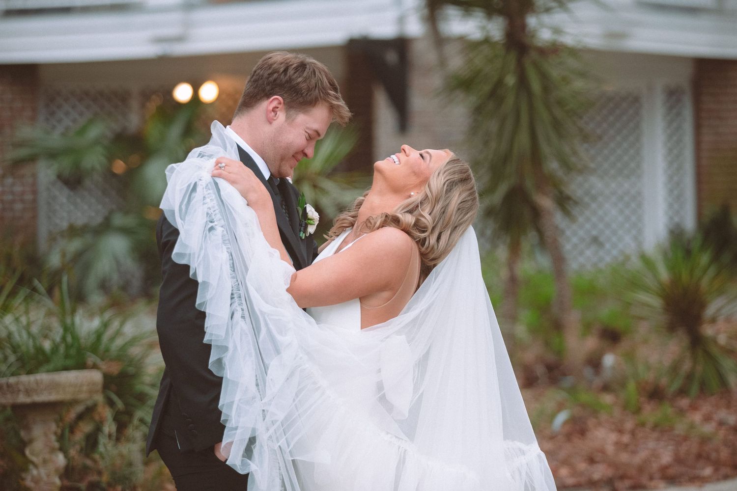 Bride and groom share a romantic moment outdoors, with her veil flowing in the wind at their wedding.