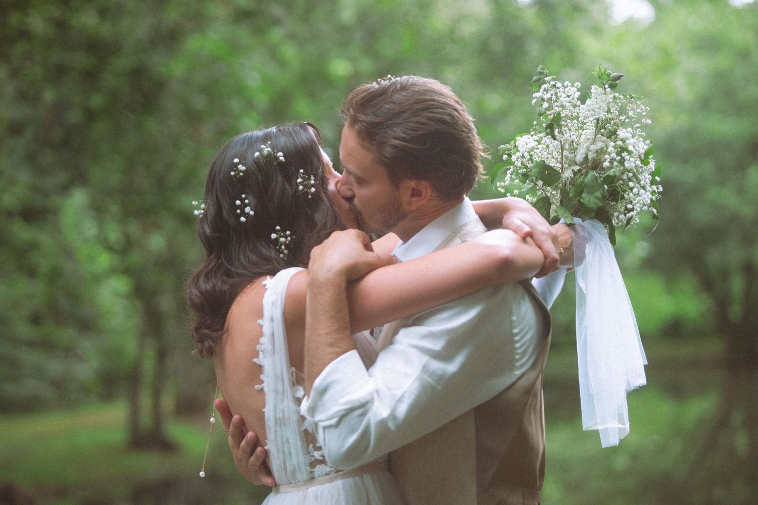 Bride and groom sharing a kiss while holding a white bouquet in a lush garden.