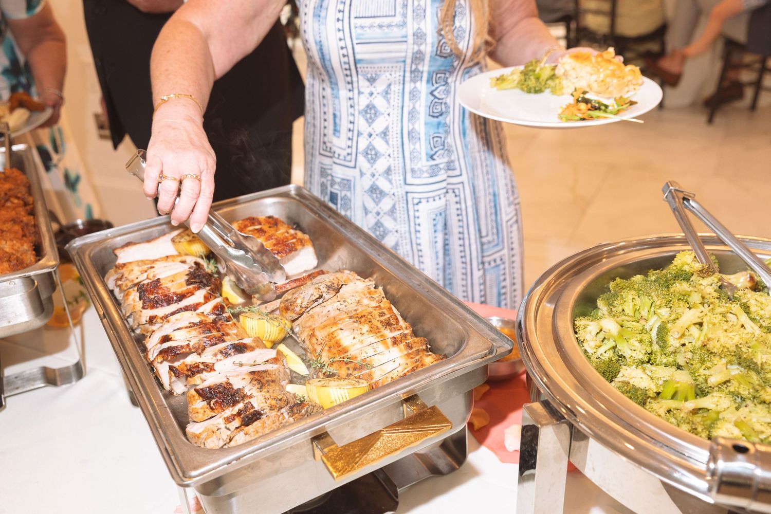 Woman using tongs to serve grilled chicken from a chafing dish at an elegant buffet.