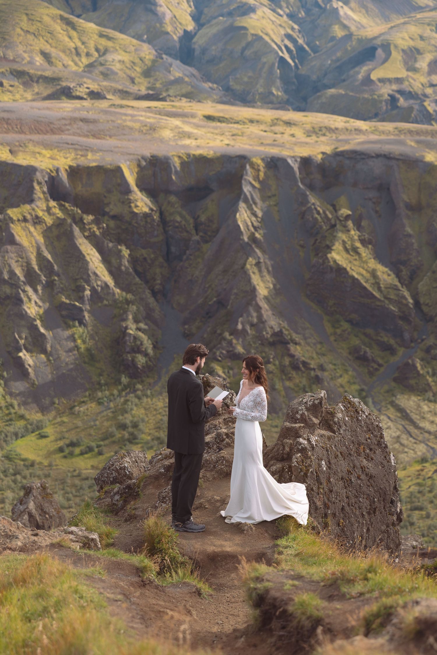 Couple exchanges wedding vows on a rocky Iceland highland cliff with stunning green mountain backdrop.