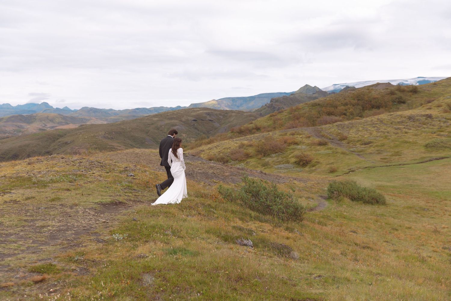 Bride and groom embrace romantically on vast green highland landscape during outdoor wedding photography session.