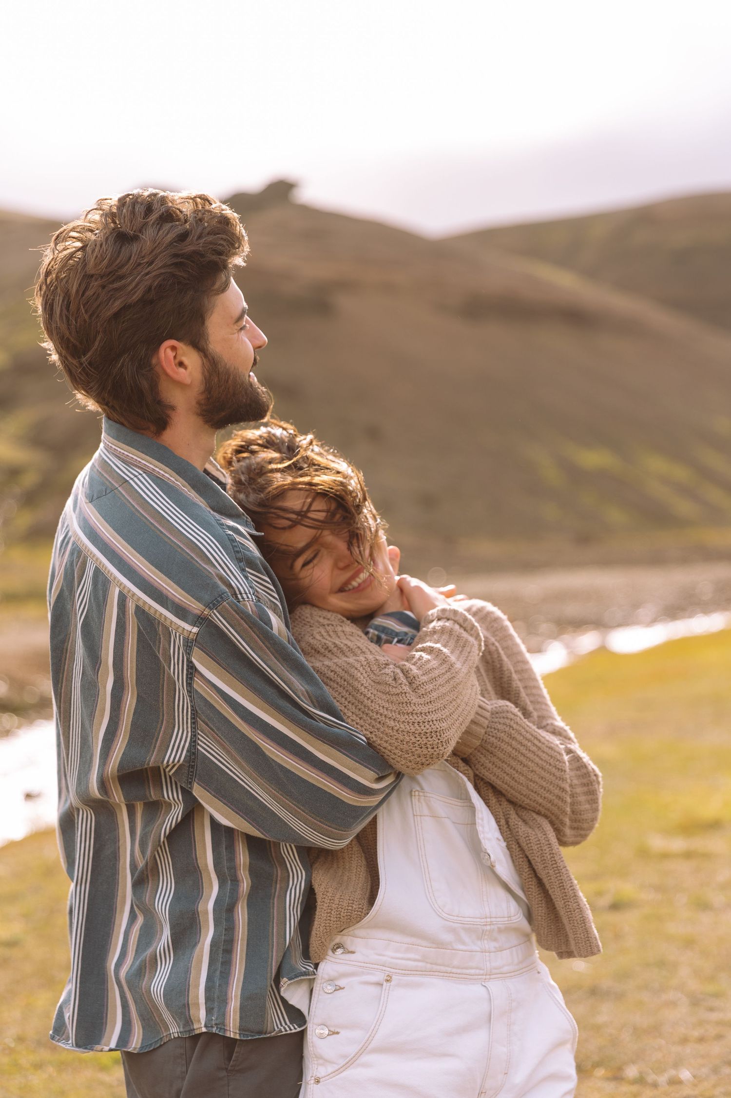 Couple embracing warmly in golden sunlight with scenic green Icelandic mountains in the background.