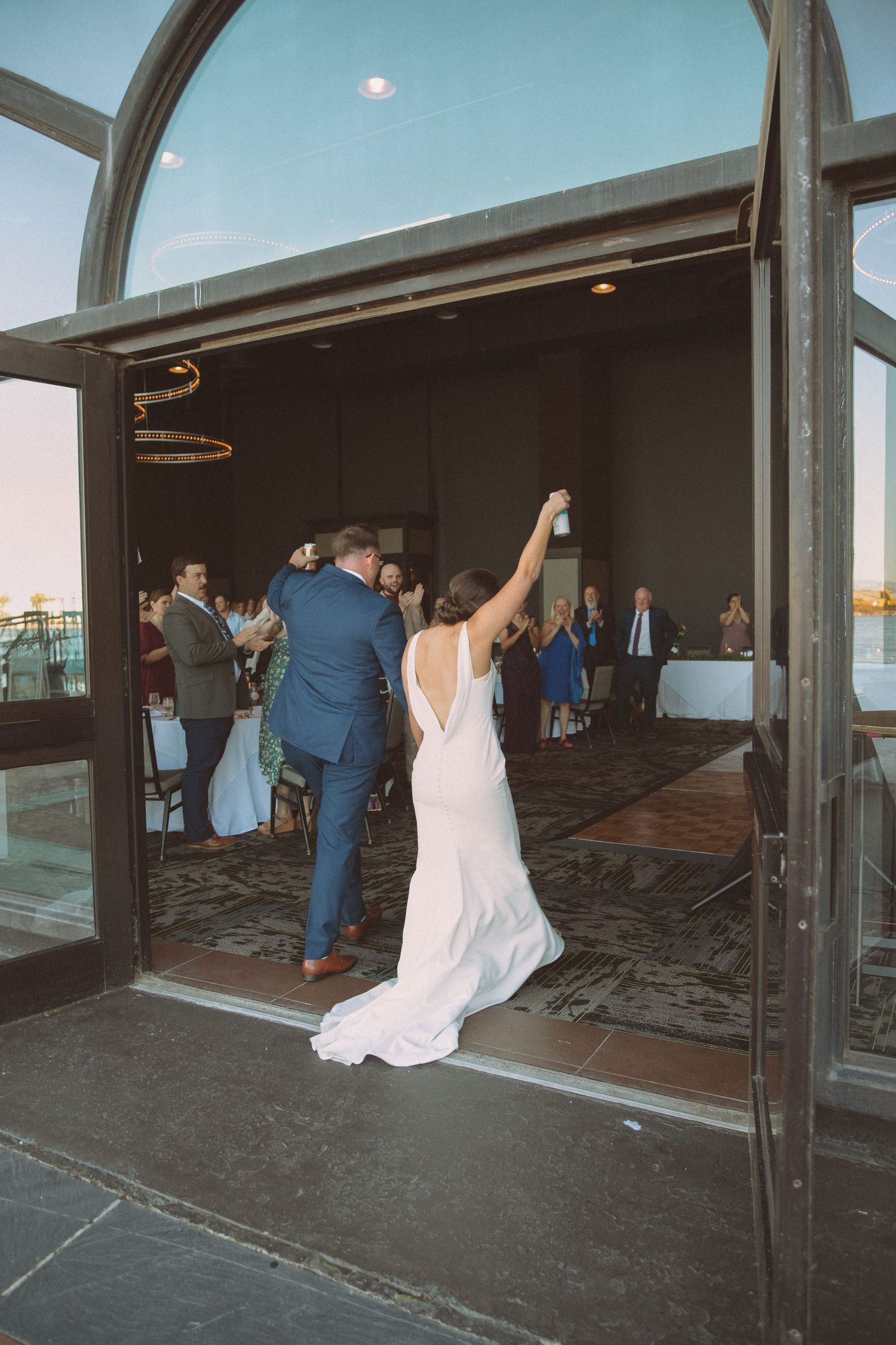 Bride raising arm triumphantly as couple makes grand entrance into waterfront wedding reception.