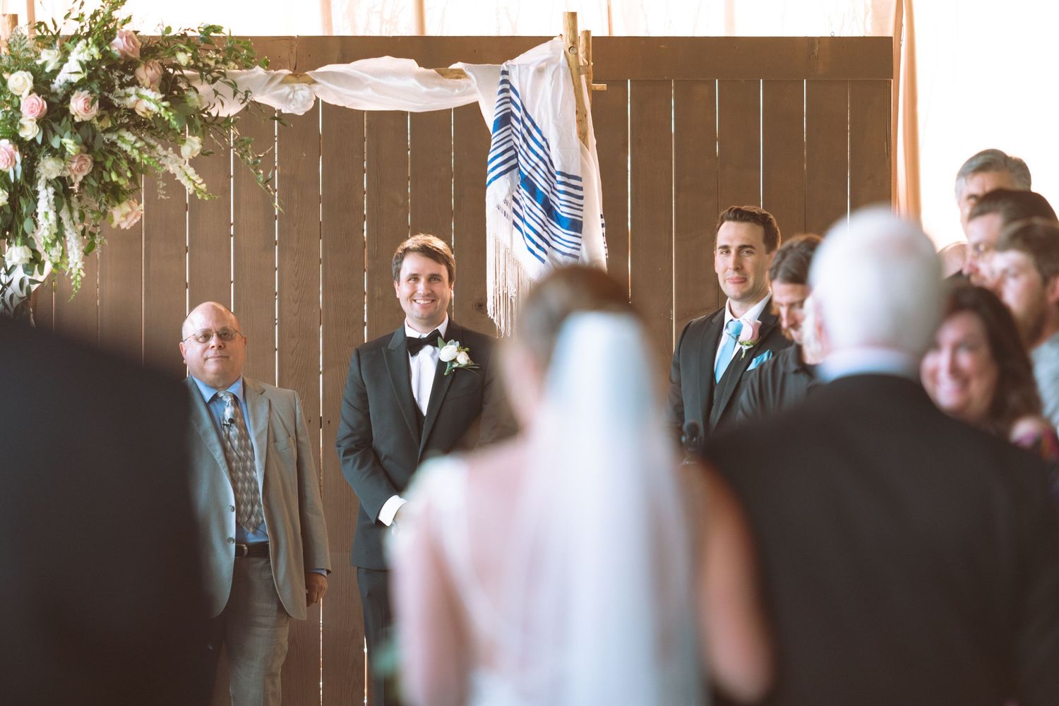 Groom smiling at bride walking down the aisle during an indoor wedding ceremony.