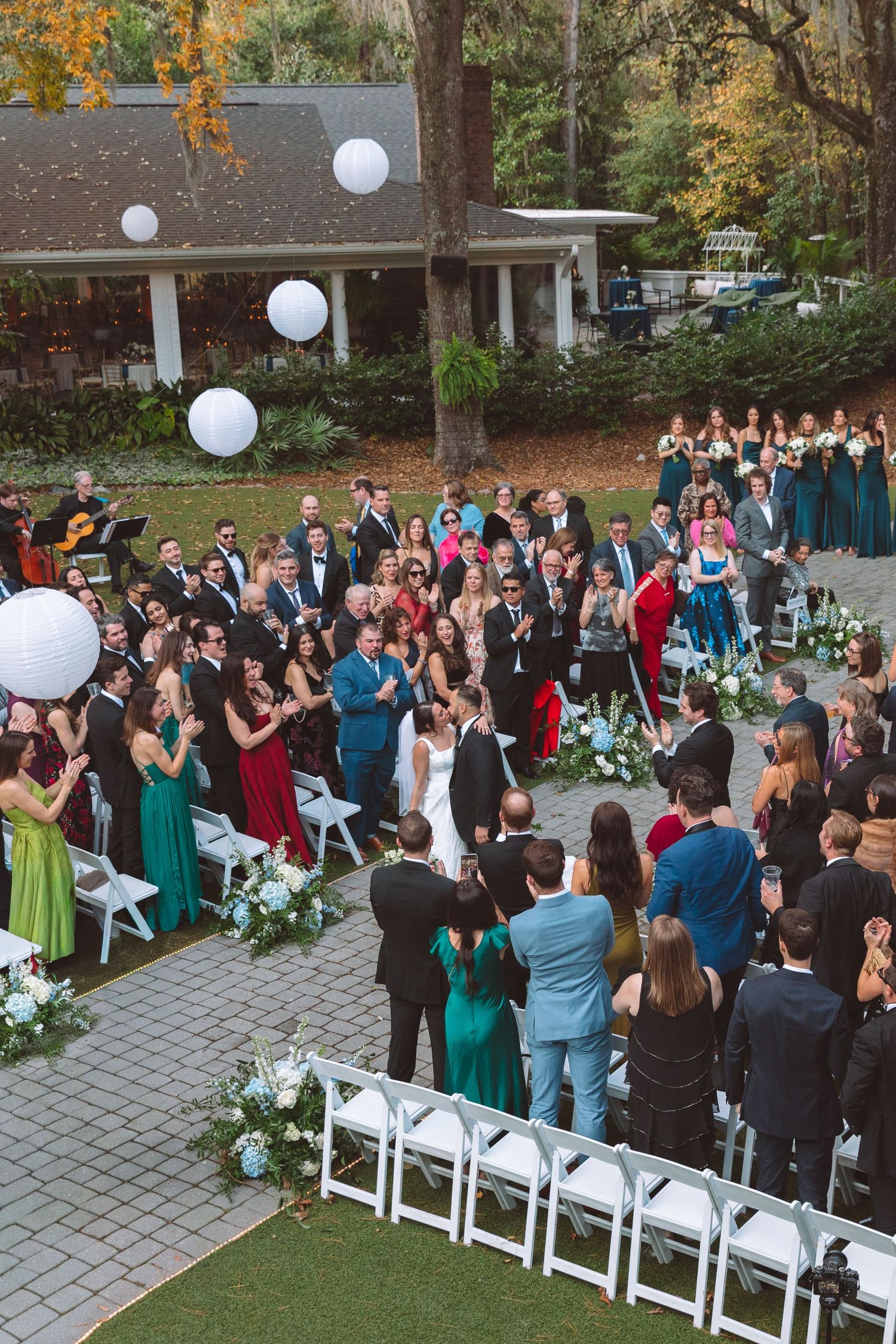 Aerial view of outdoor wedding ceremony with guests applauding newlyweds on stone patio.