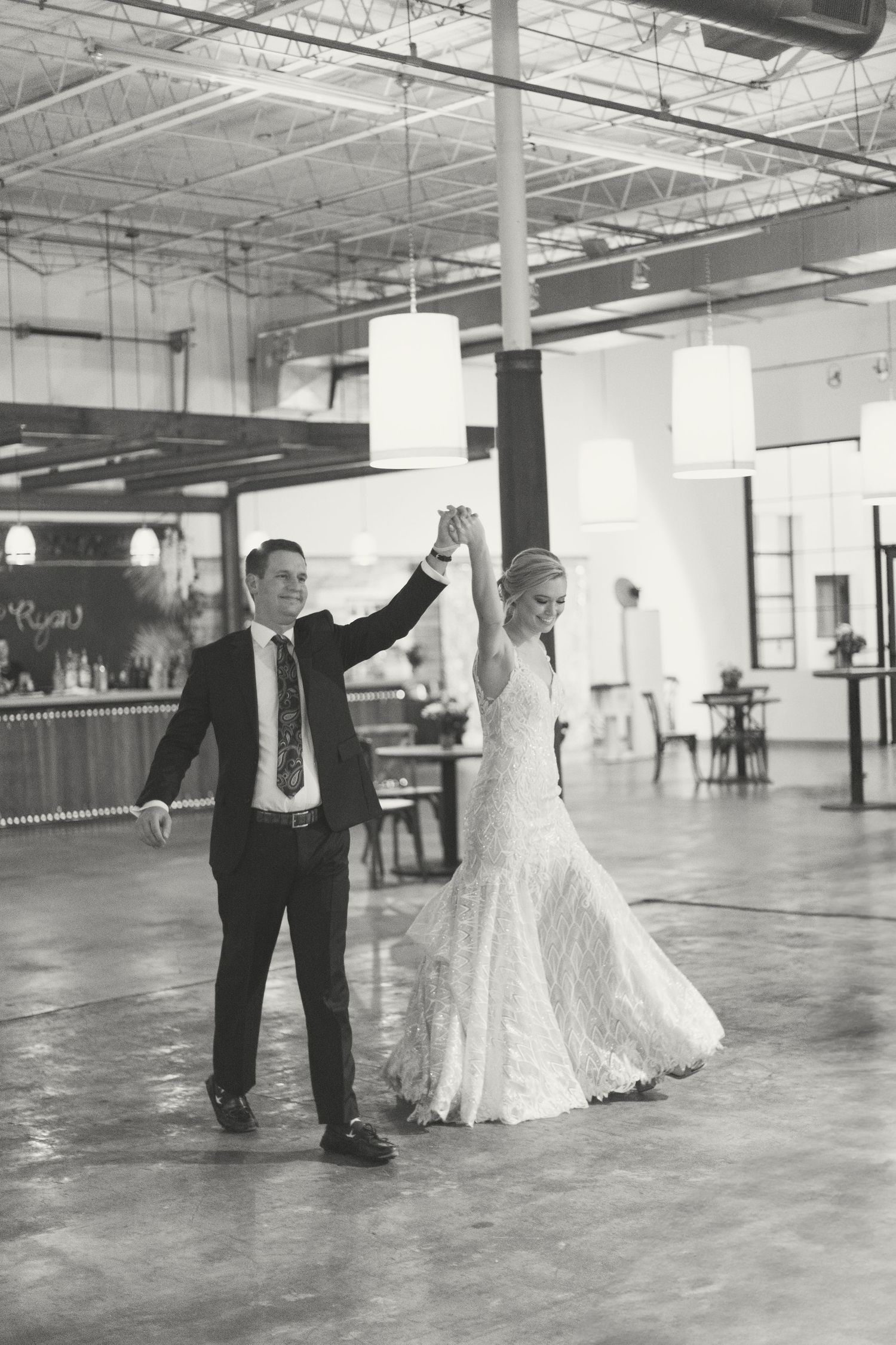 Black and white photo of bride and groom sharing first dance in elegant industrial wedding venue.