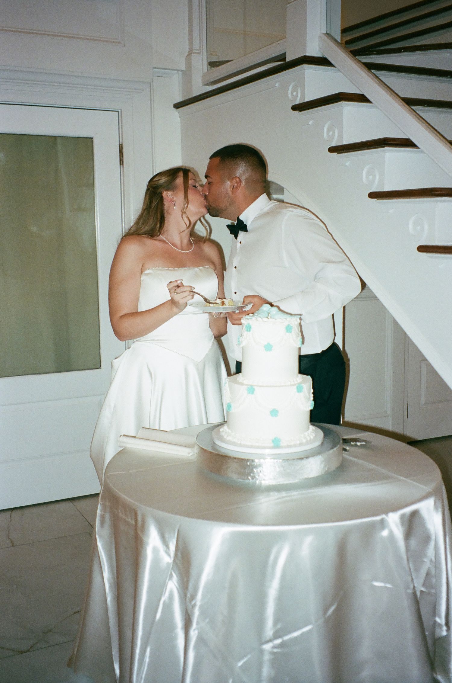 Newlyweds kissing while cutting their white polka dot wedding cake at indoor reception venue.