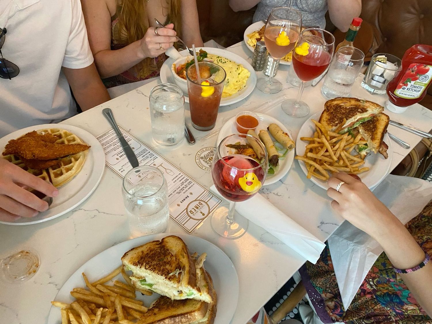 Group dining table with sandwiches, french fries, cocktails and water glasses at restaurant.