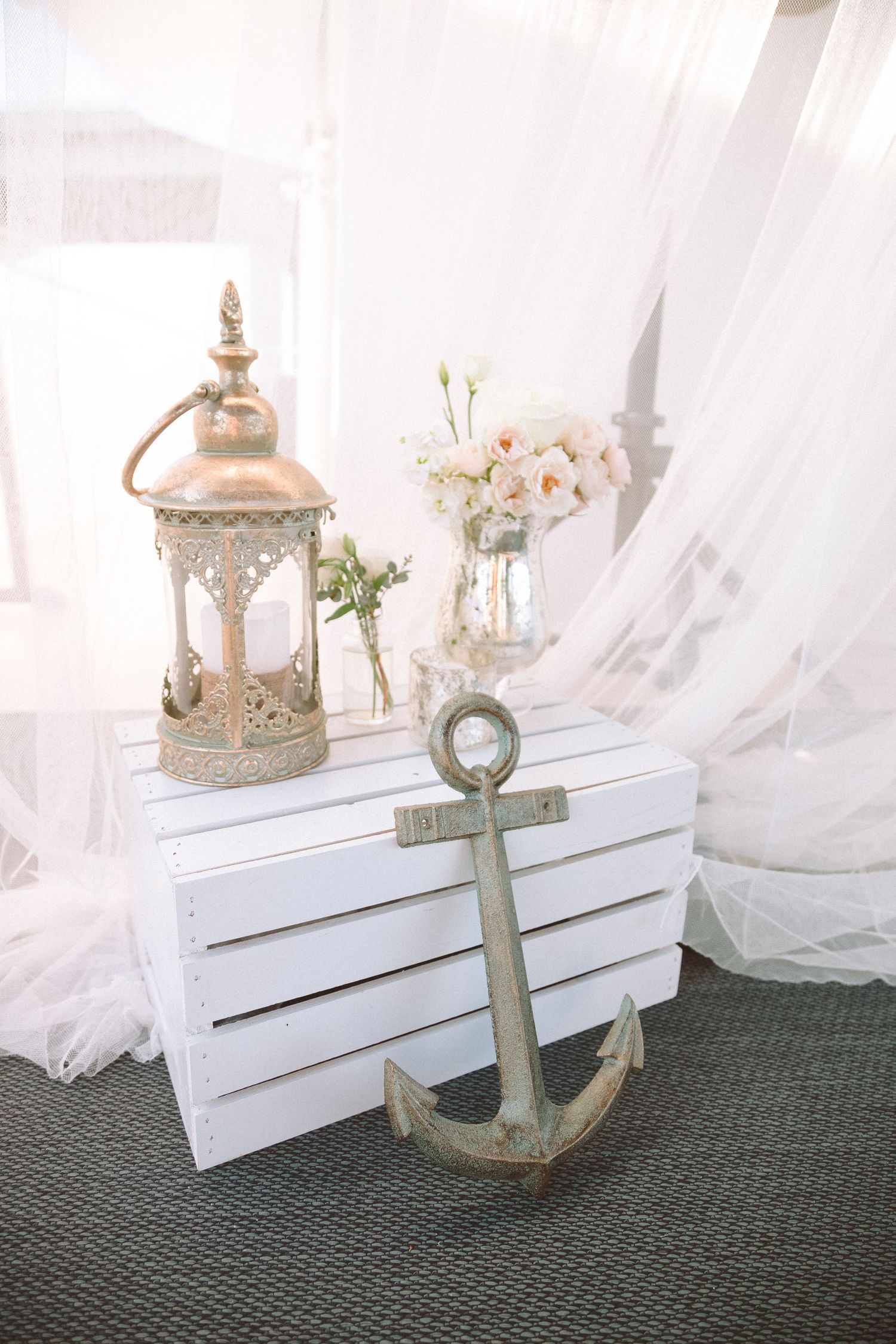 Elegant nautical wedding decor featuring a vintage anchor, lantern, and white roses on a white wooden crate.