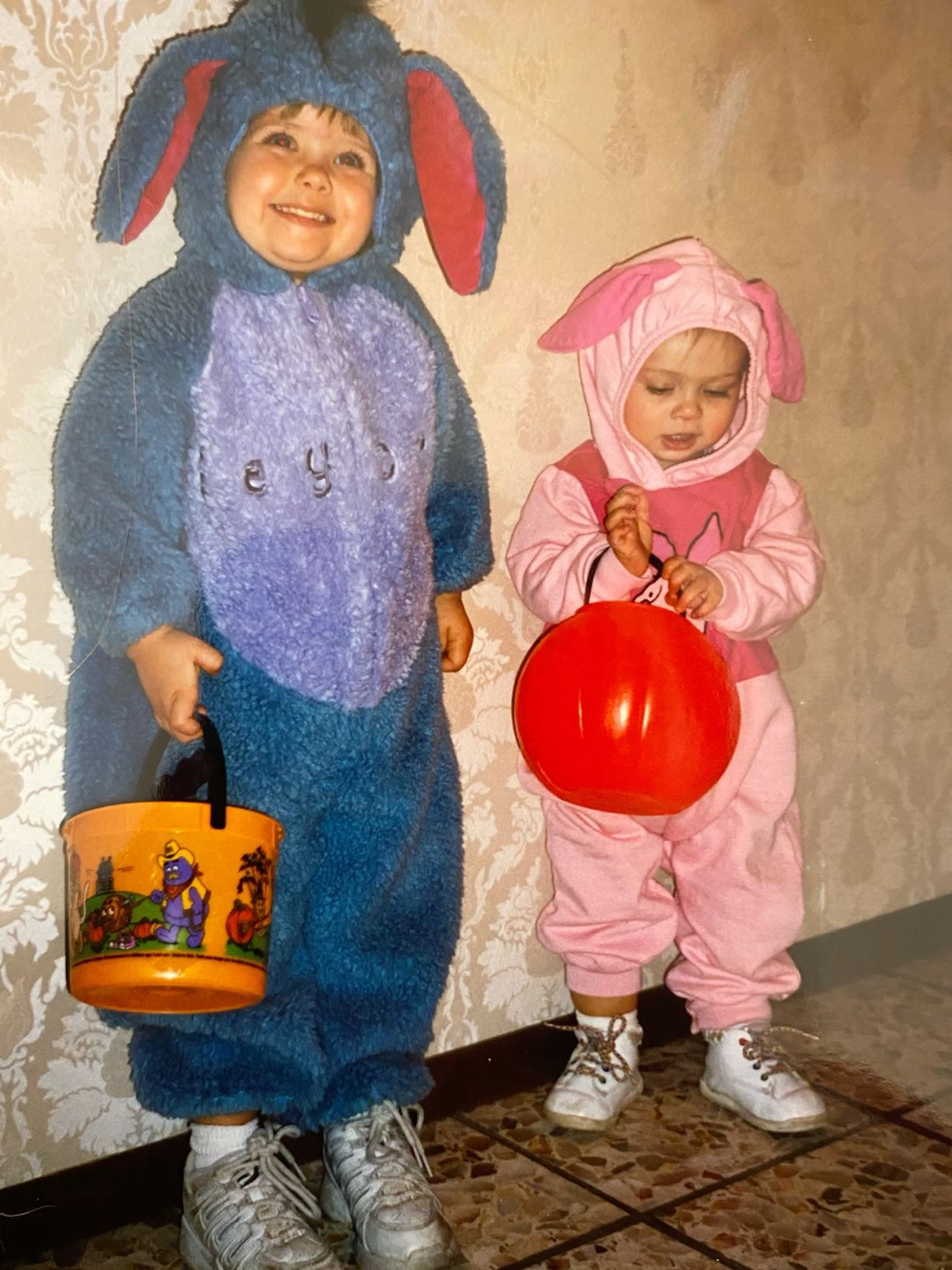 Two toddlers in Eeyore and Piglet Halloween costumes hold trick-or-treat buckets.