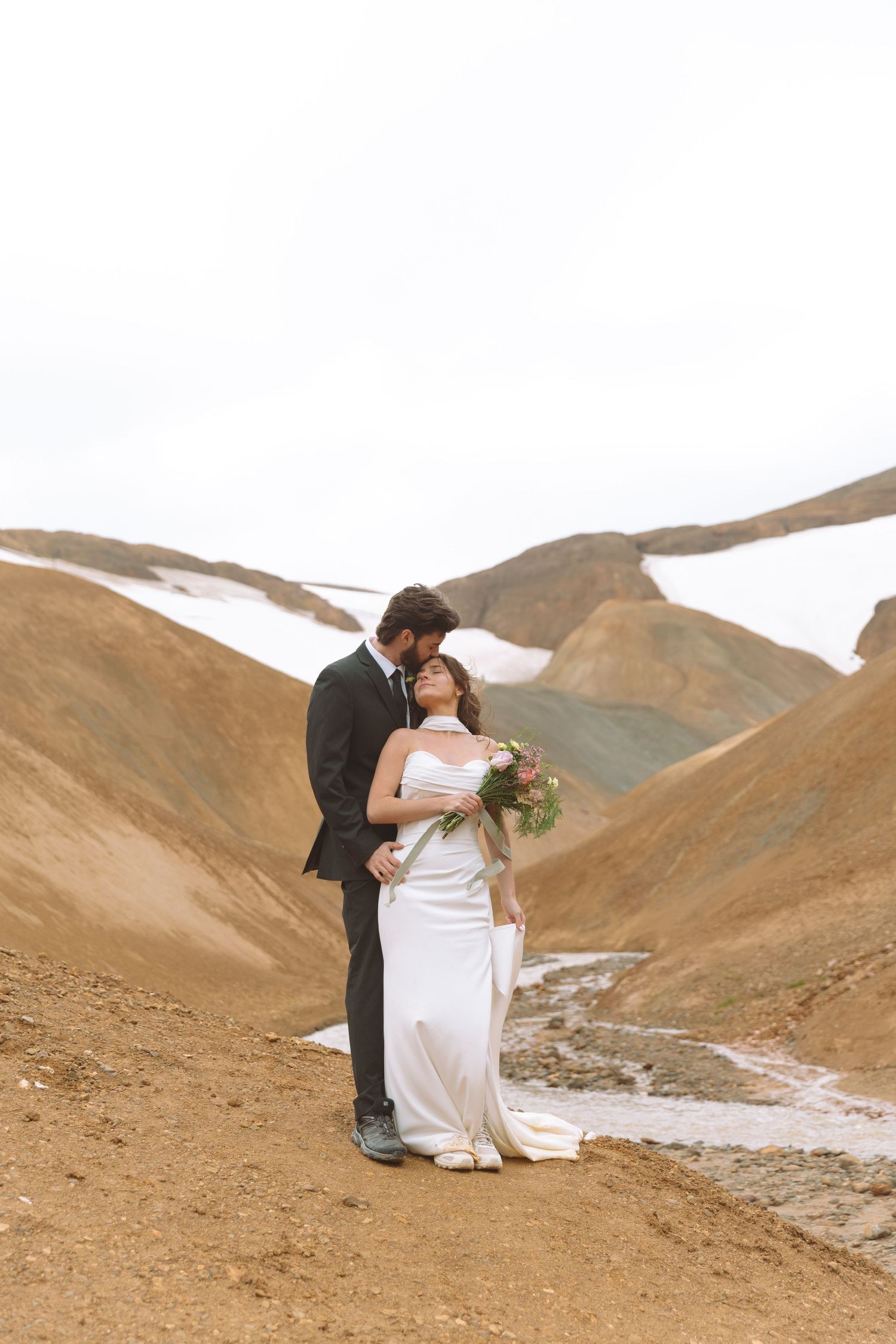 Groom kisses bride as she tilts her head back joyfully on a scenic mountain elopement in Iceland.