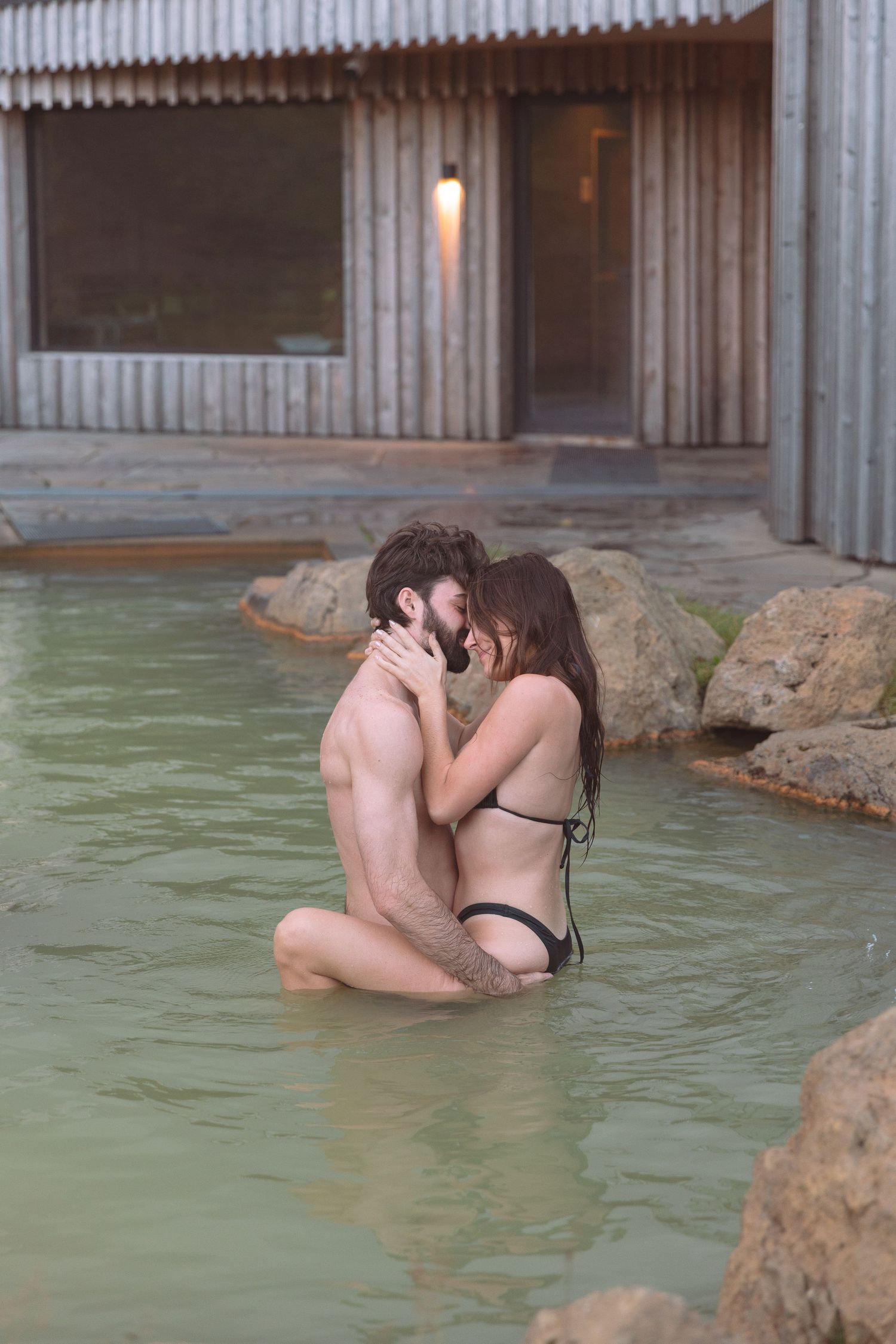 Couple sharing a passionate kiss while kneeling in a warm geothermal pool.