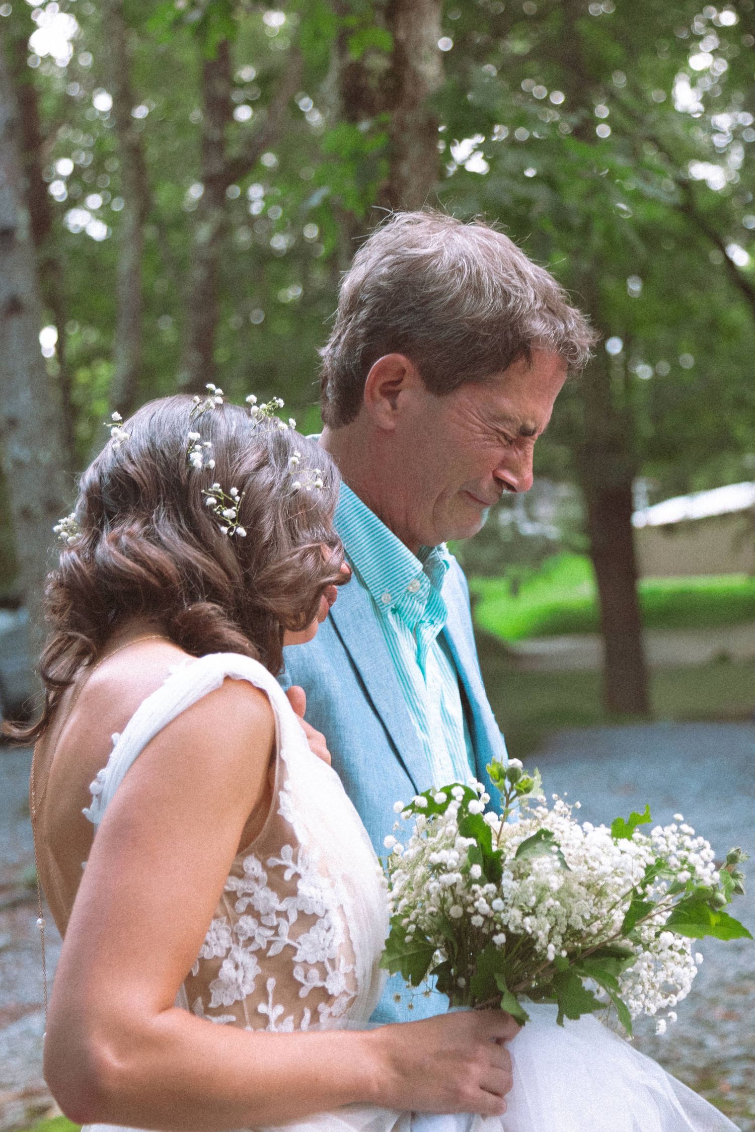 Bride with floral hair accessories holding white bouquet standing with older man outdoors.
