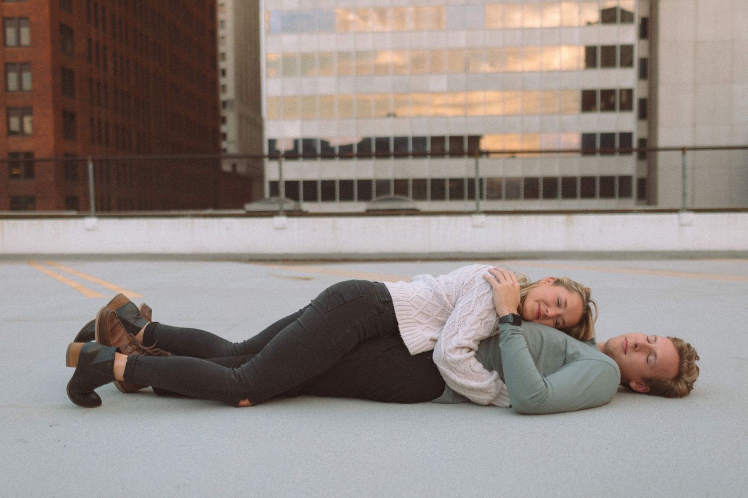 Couple lying on a rooftop together with city buildings in the background.