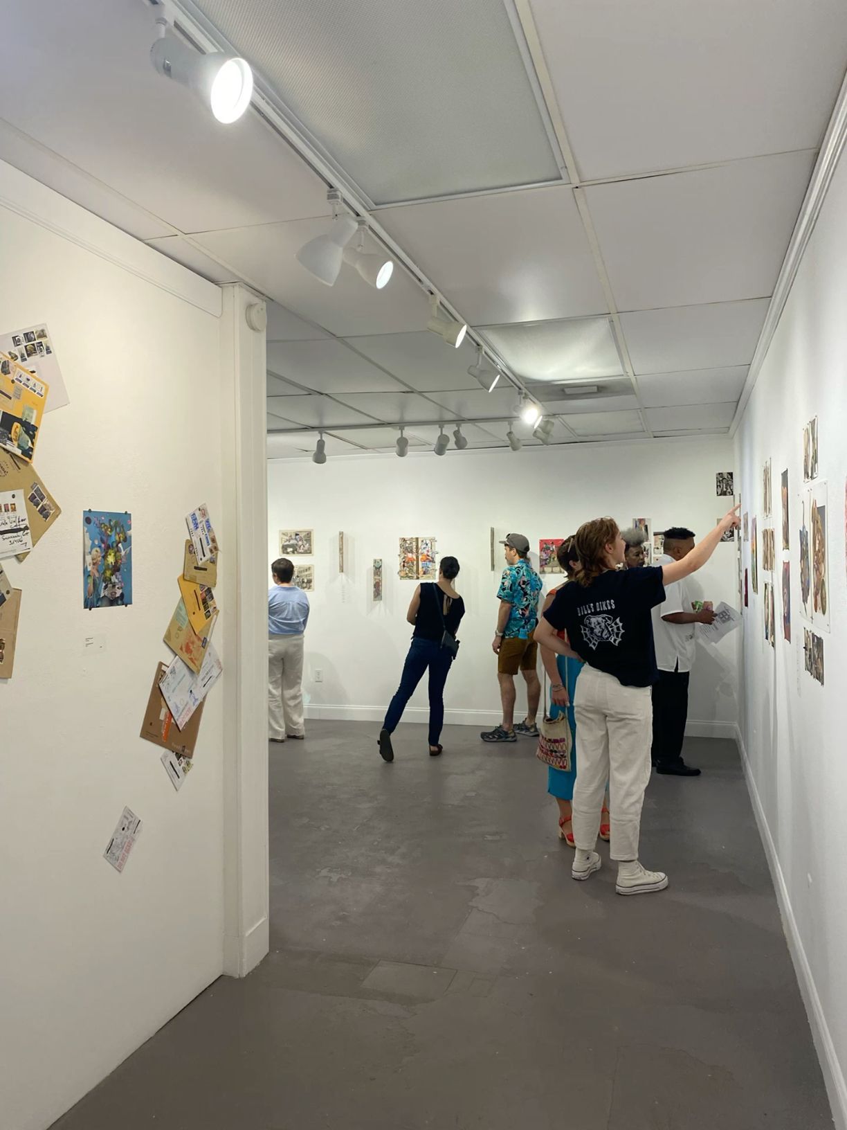 Visitors browsing colorful artwork displayed on white gallery walls in a well-lit contemporary art exhibition space.