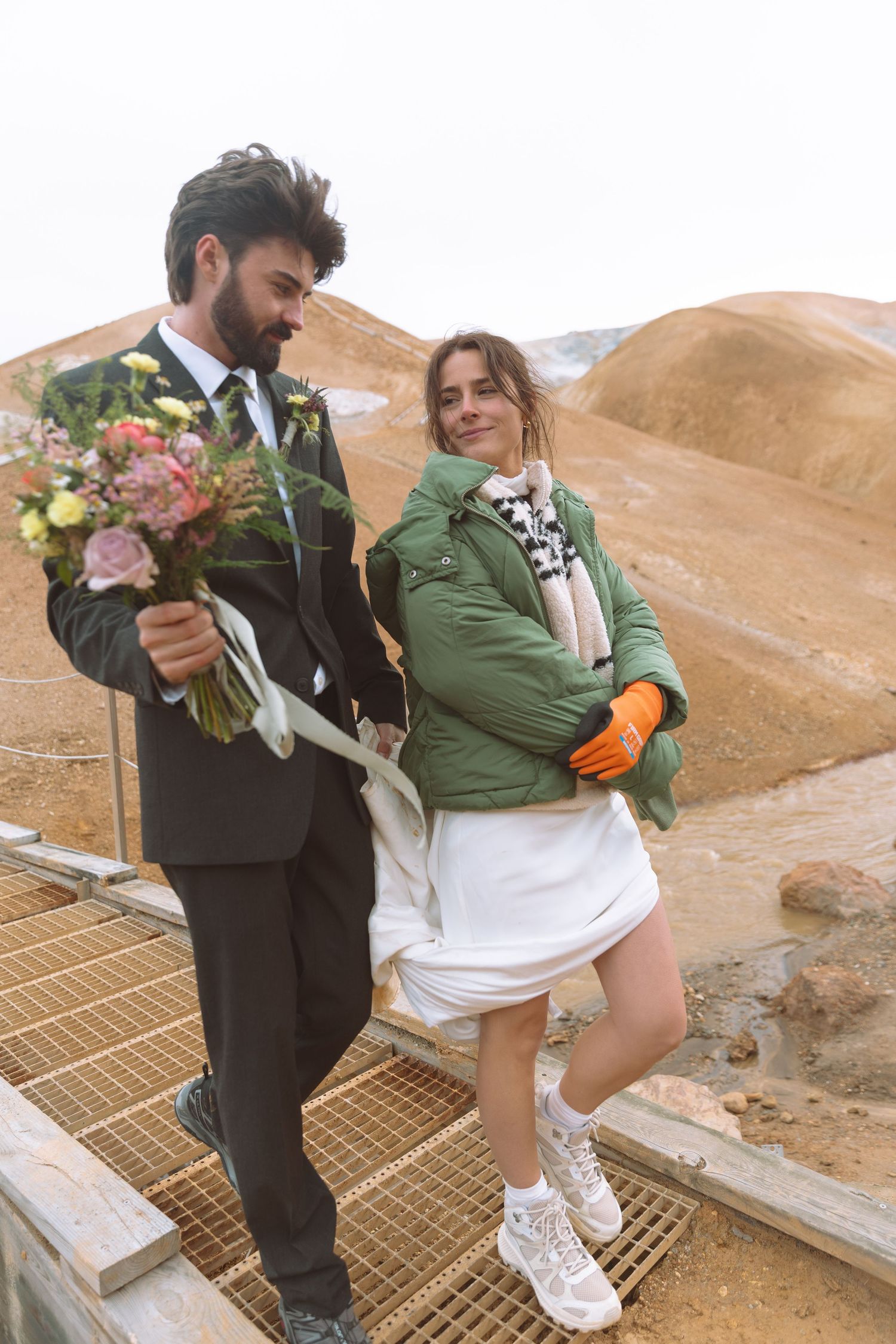 Couple poses on a wooden bridge surrounded by golden rhyolite mountains during Iceland wedding shoot.