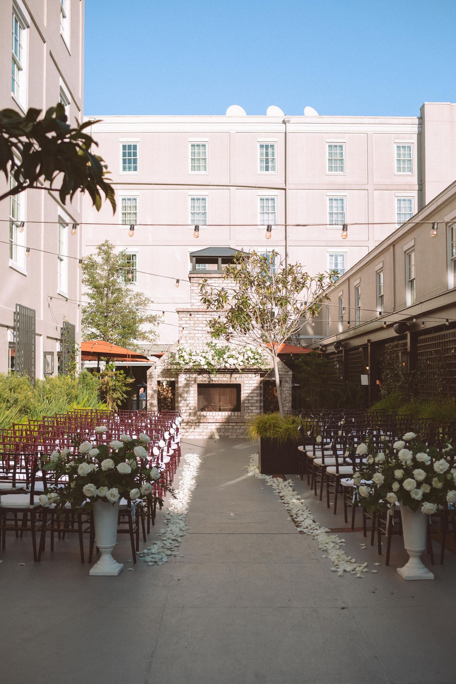 Elegant outdoor wedding ceremony setup with white floral arrangements lining the aisle in a courtyard.