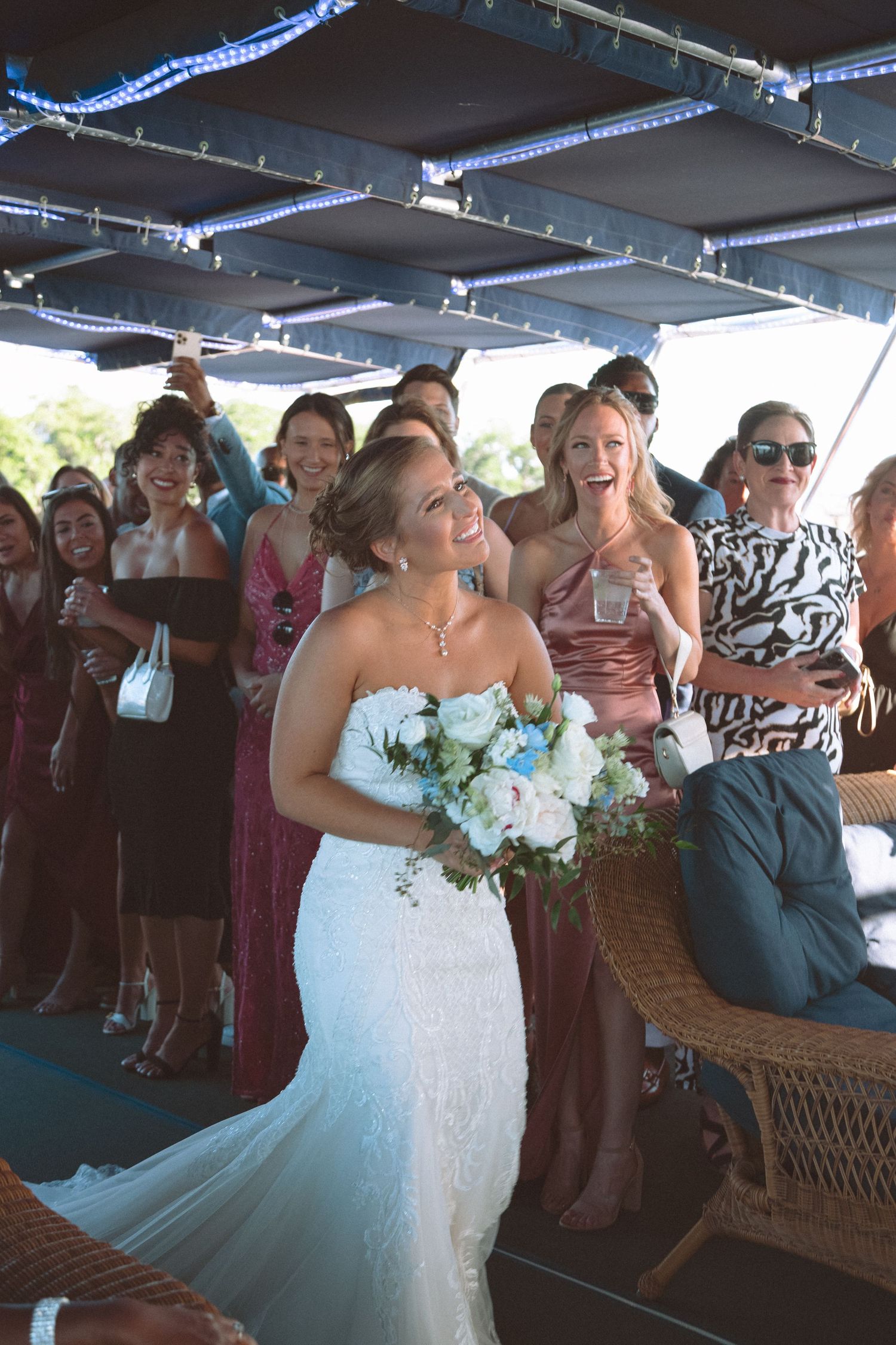 Smiling bride in lace gown prepares to toss bouquet to excited wedding guests.