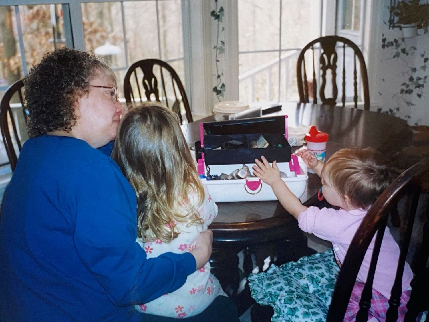 A curly-haired woman sits with two young girls at a dining table doing an activity.