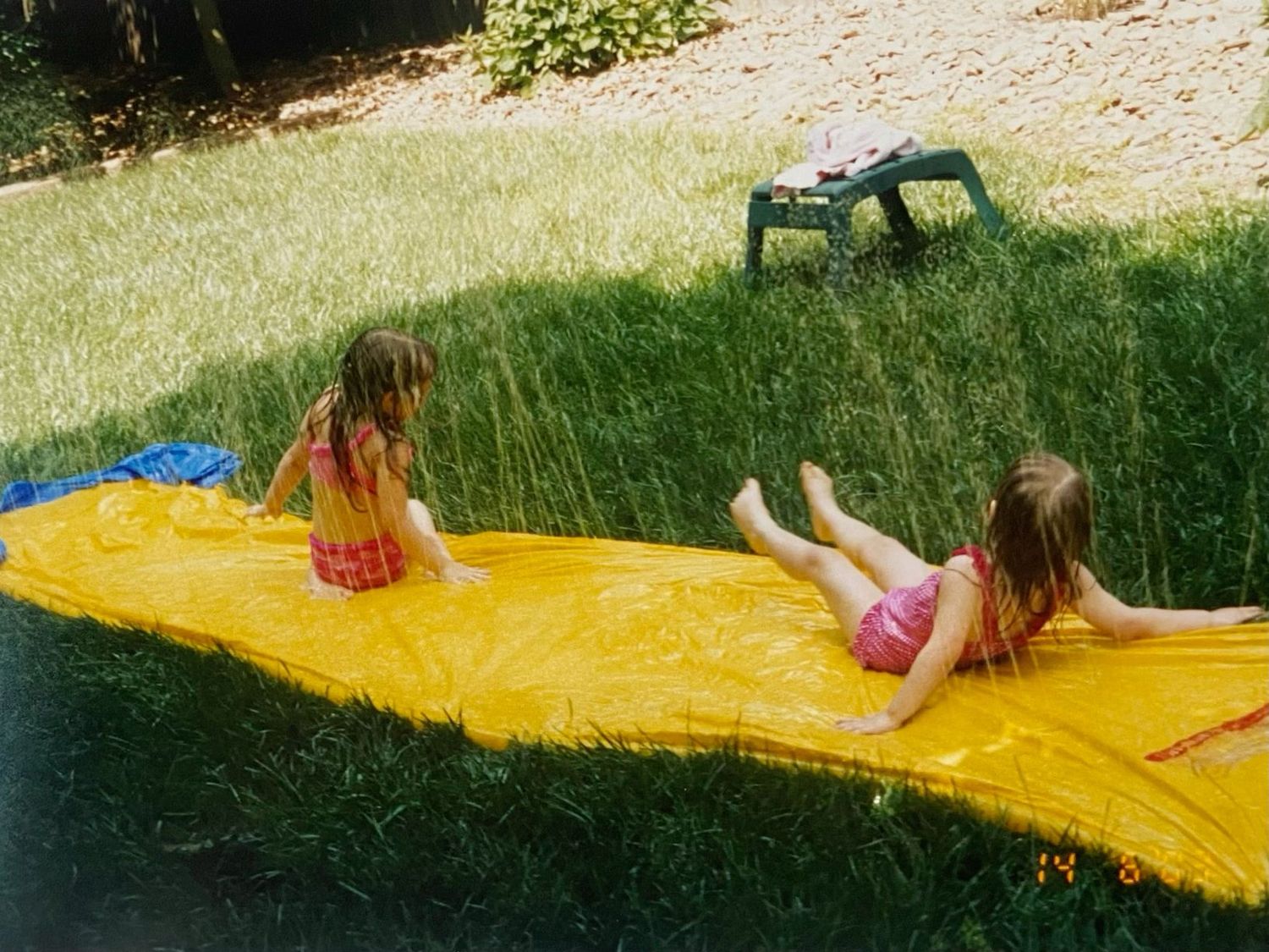 Two young girls playing on a yellow slip and slide in a backyard.