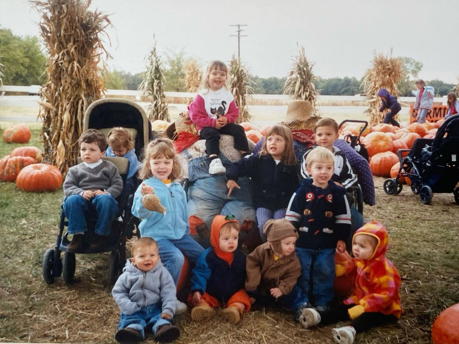 Group of young children posing with pumpkins at a fall harvest pumpkin patch outdoor event.