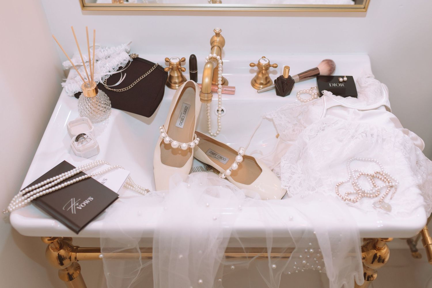 Elegant bridal accessories including pearl heels, jewelry, veil, and cosmetics arranged on marble vanity.