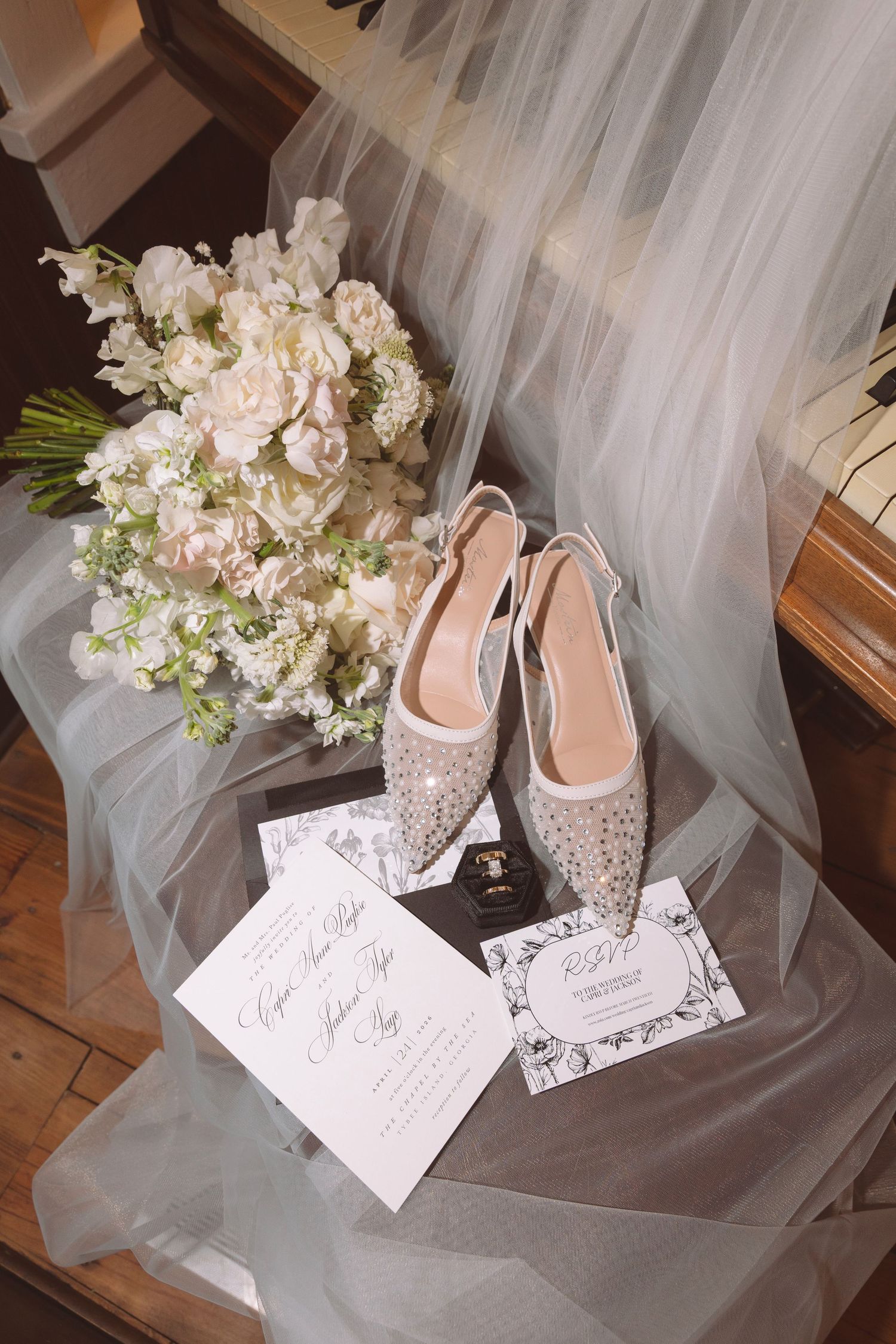 Elegant bridal flat shoes with crystal embellishments displayed with wedding invitations and white floral bouquet.