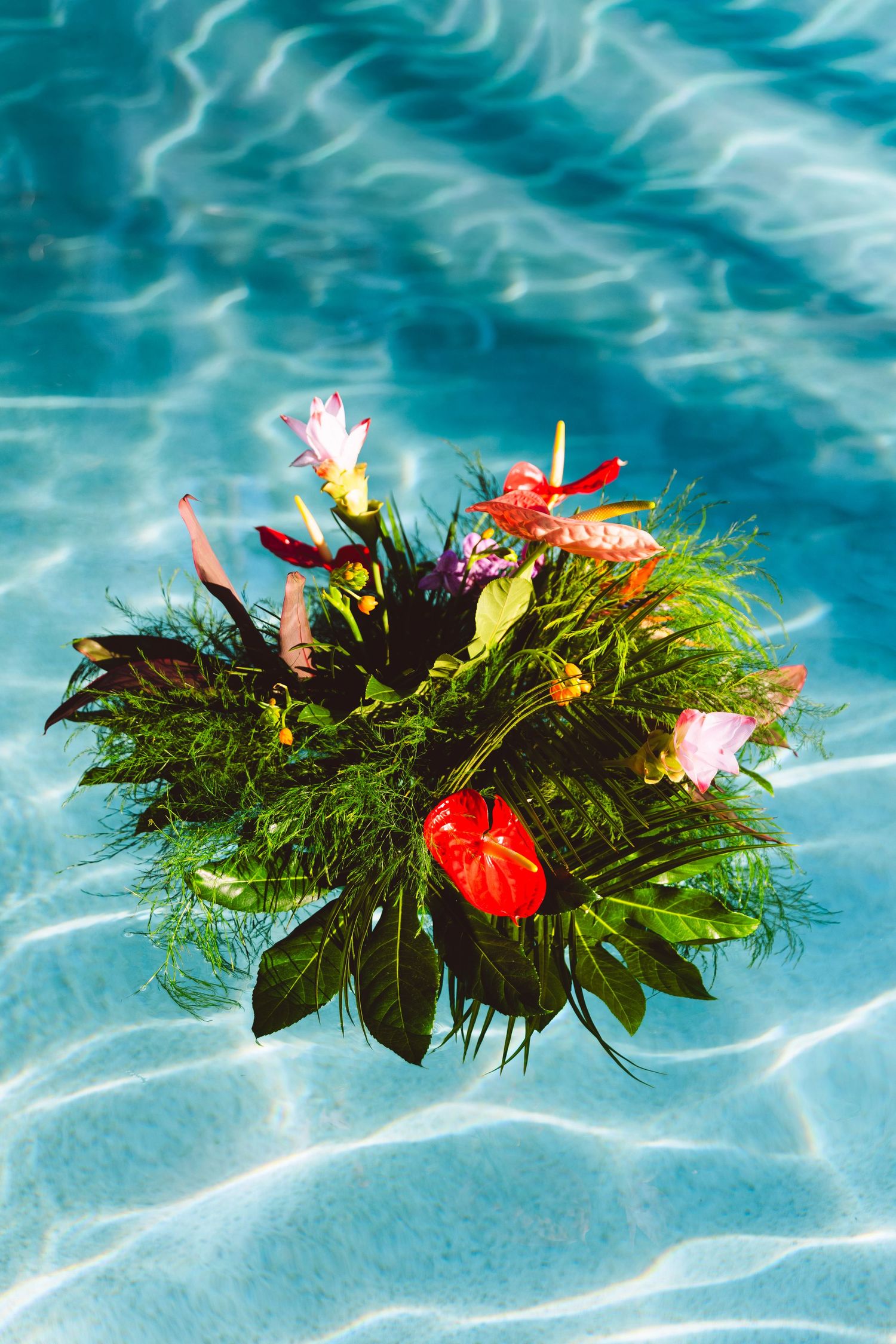 Colorful tropical flower arrangement floating in a crystal clear blue swimming pool.