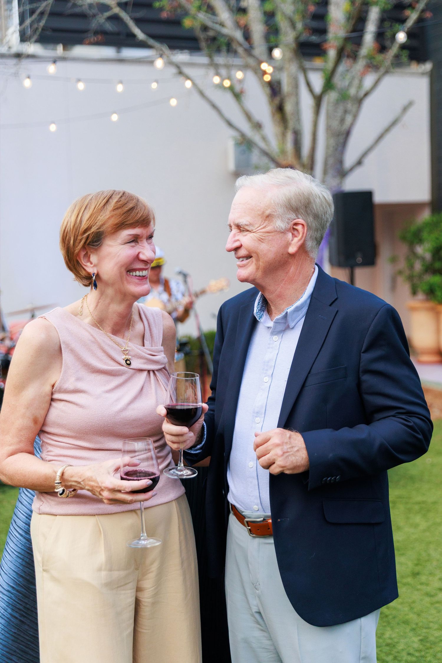 Smiling senior couple enjoying red wine at an outdoor evening garden party with string lights.