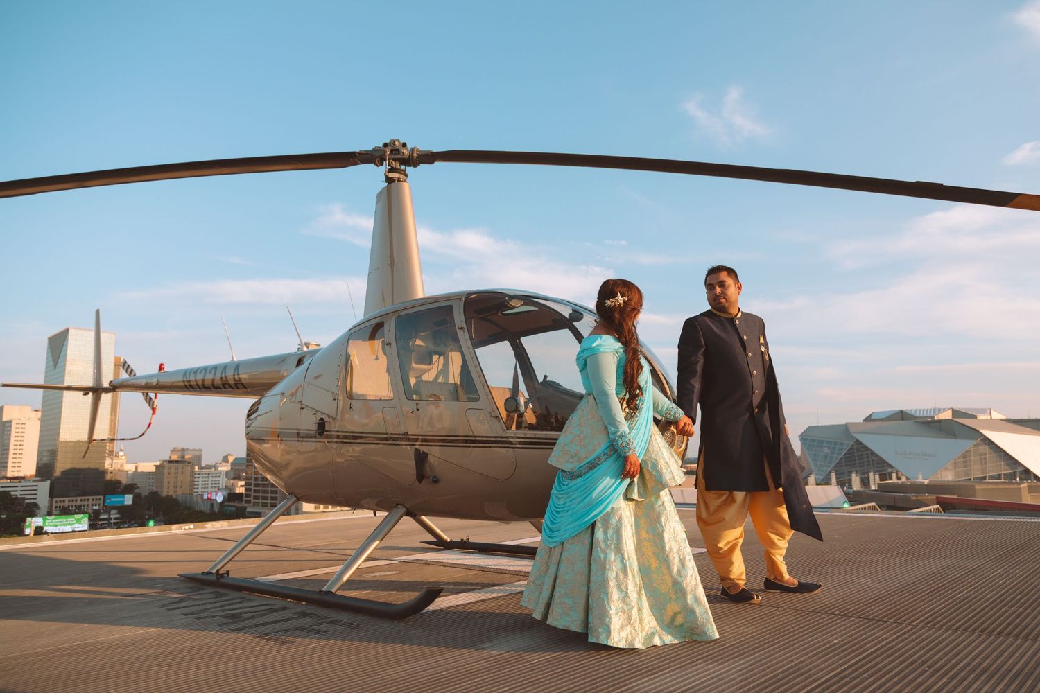 Couple in traditional South Asian wedding attire posing in front of a helicopter.