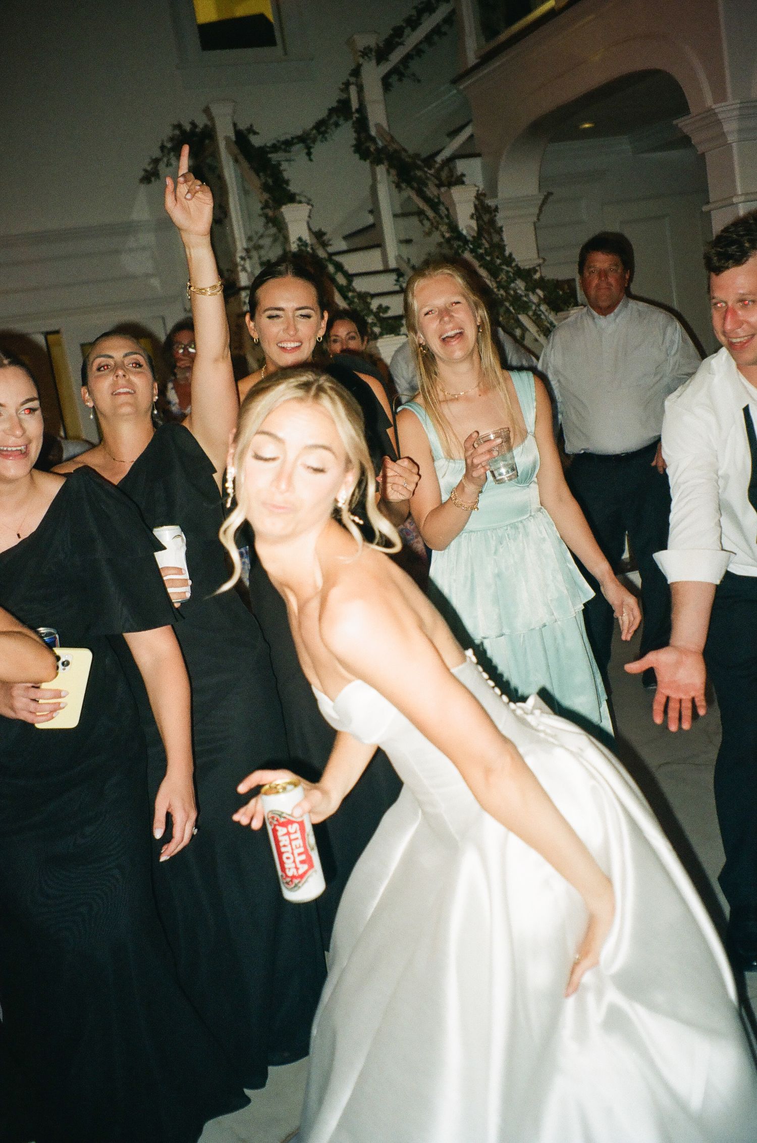 Bride in white gown dancing energetically with guests at a lively wedding reception.