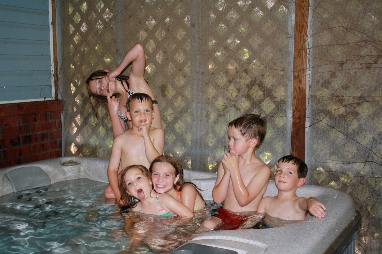Group of children laughing and playing together in a steaming outdoor hot tub at night.