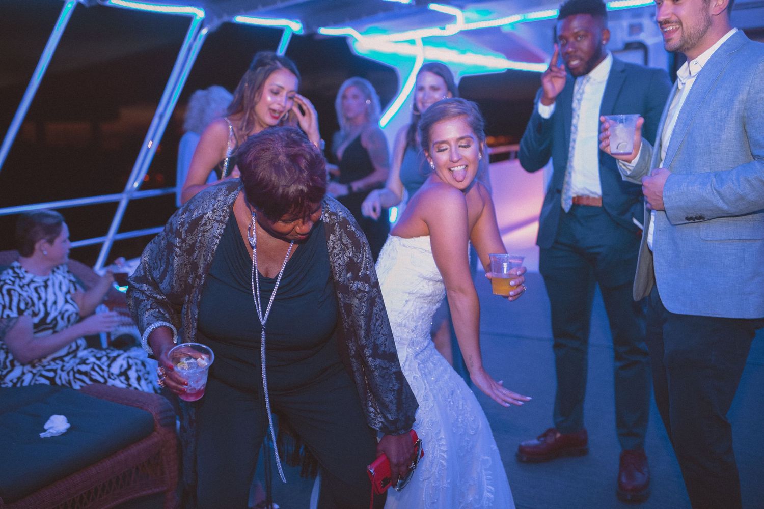 Bride in white wedding dress smiles while dancing with older female guest at wedding reception.