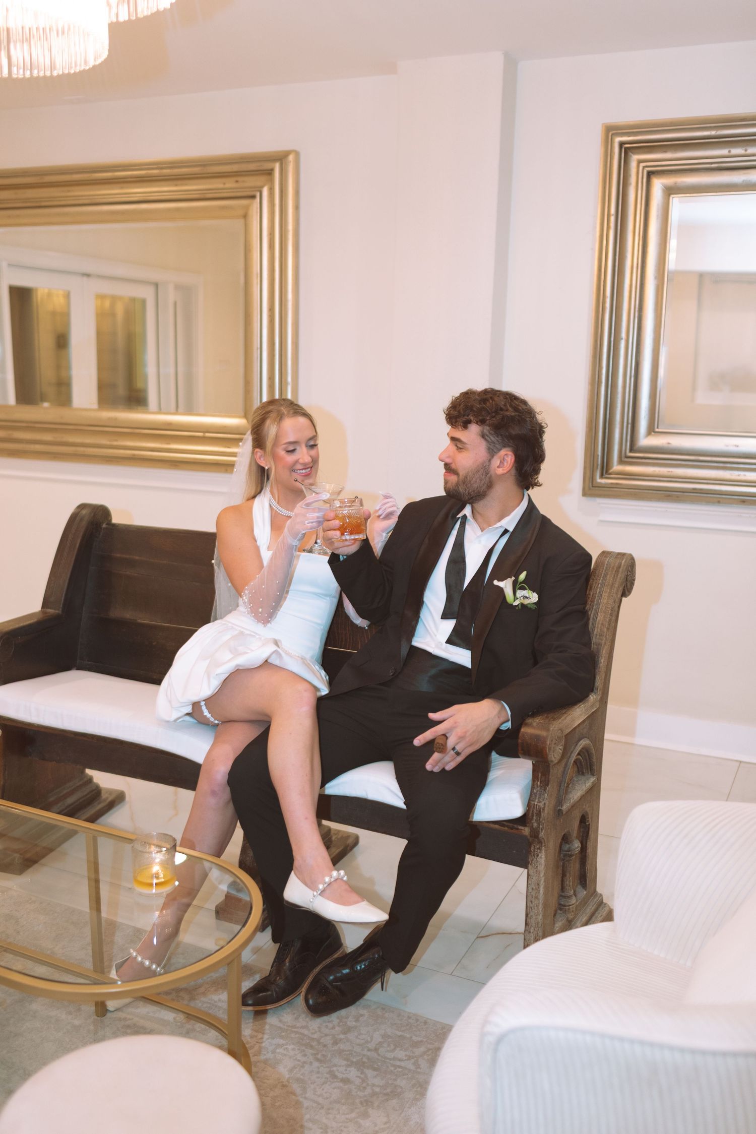 Bride and groom toasting drinks together while seated on a bench at their wedding reception.
