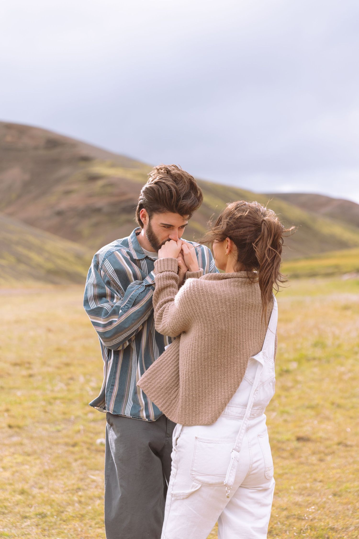 Bearded man kissing womans hands while standing together in a scenic green meadow.