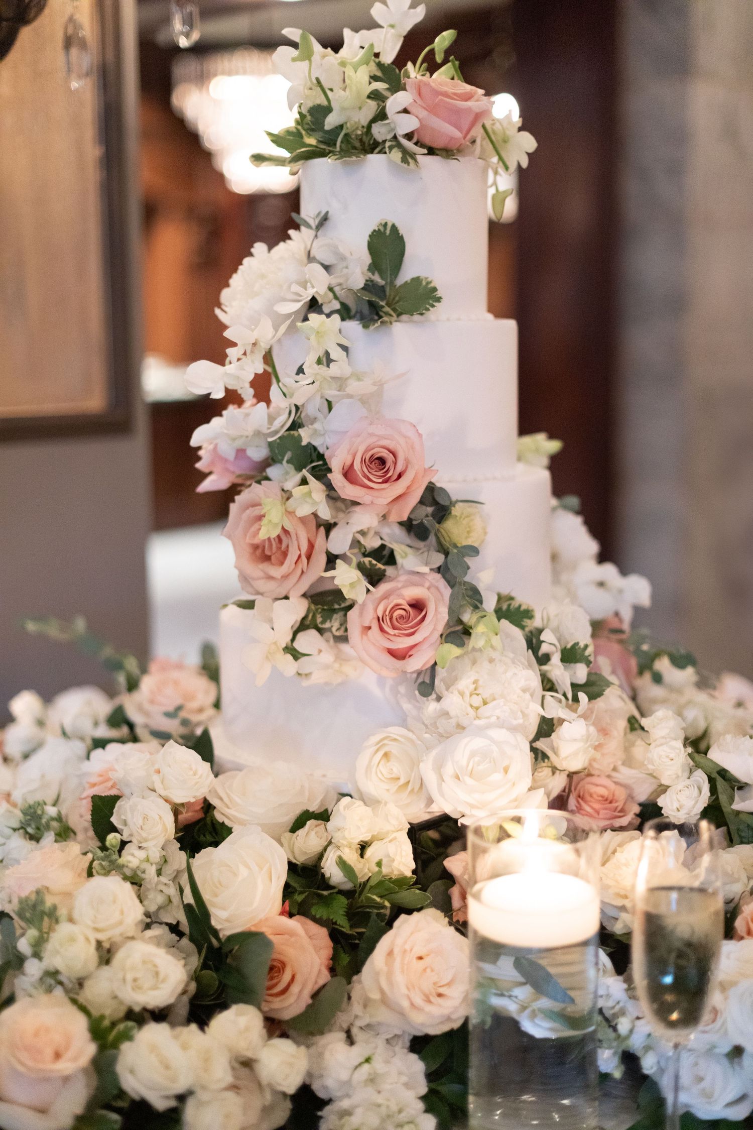 Elegant four-tier white wedding cake adorned with cascading pink and white roses and candles.