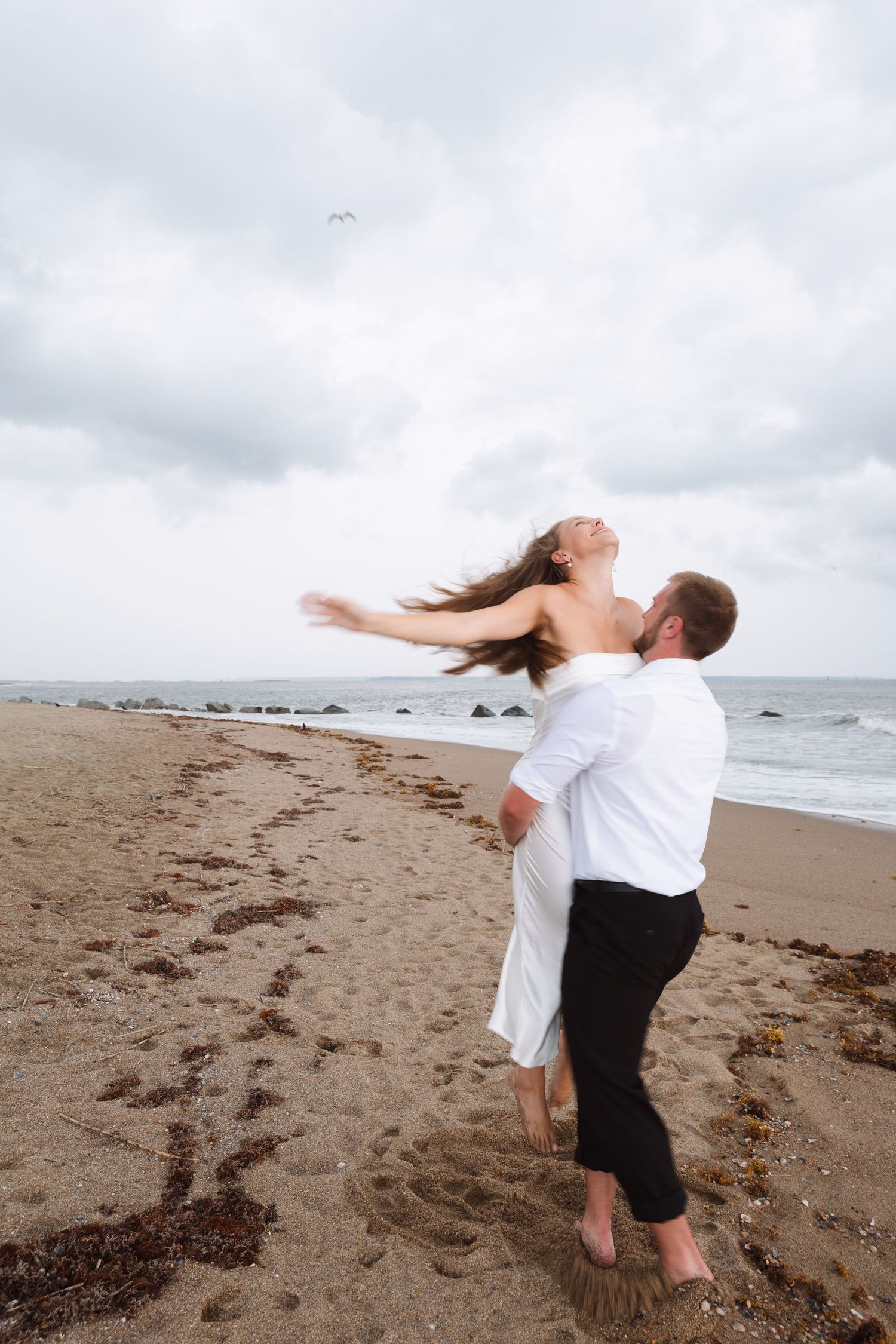 Man lifting woman on a sandy beach, her hair flowing as she leans back joyfully.