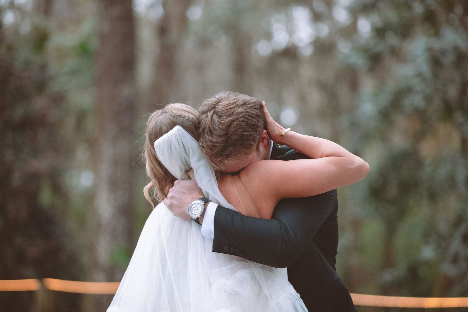 Bride and groom share emotional embrace during outdoor first look surrounded by trees.