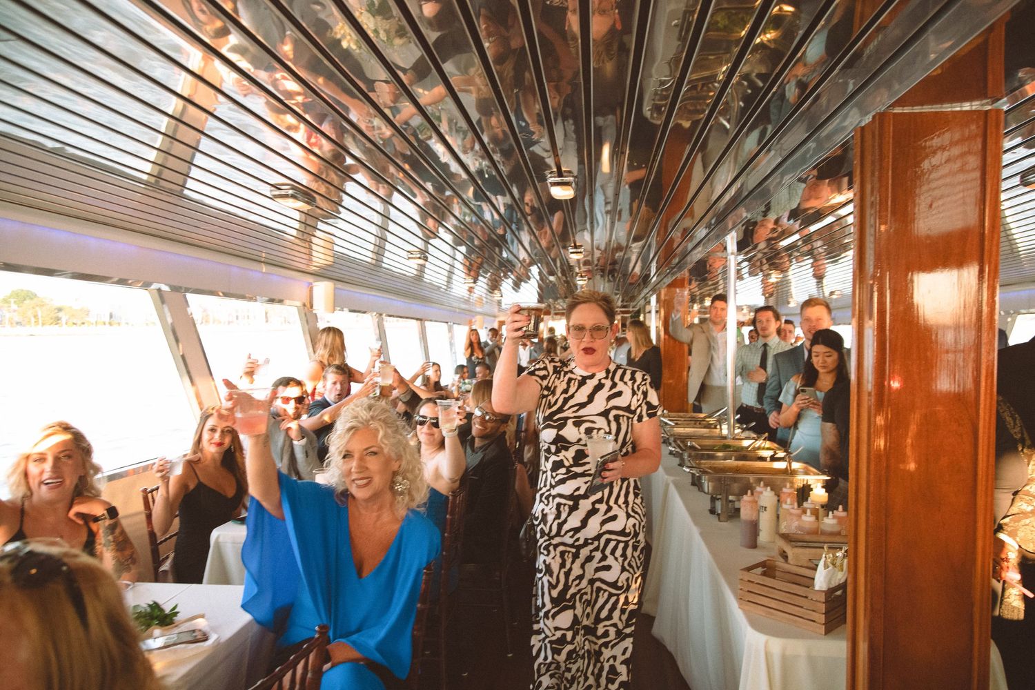 Wedding guests raising glasses in a celebratory toast during a boat reception with buffet dining.
