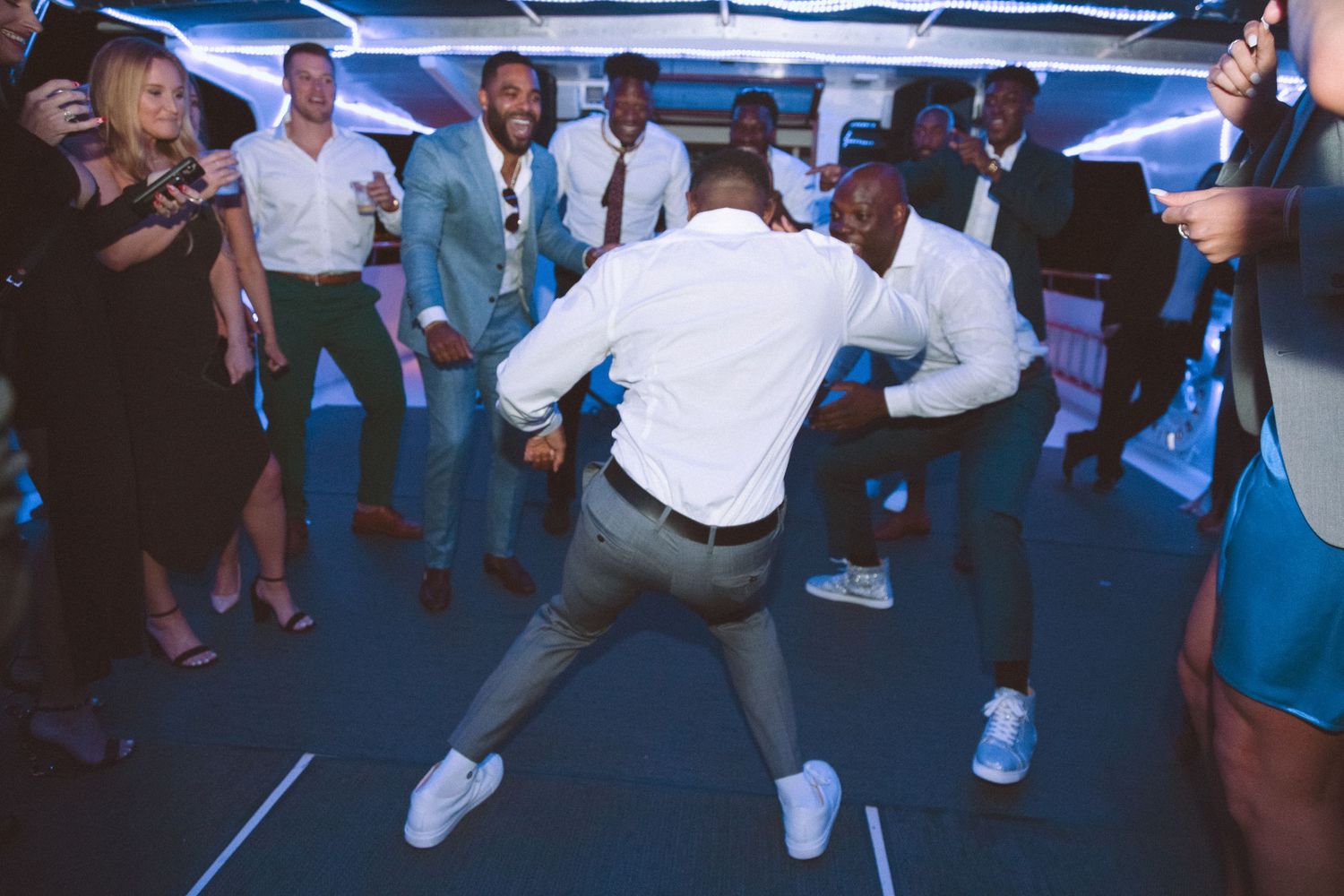 Two men showcasing impressive dance moves at a wedding reception while guests watch and cheer.