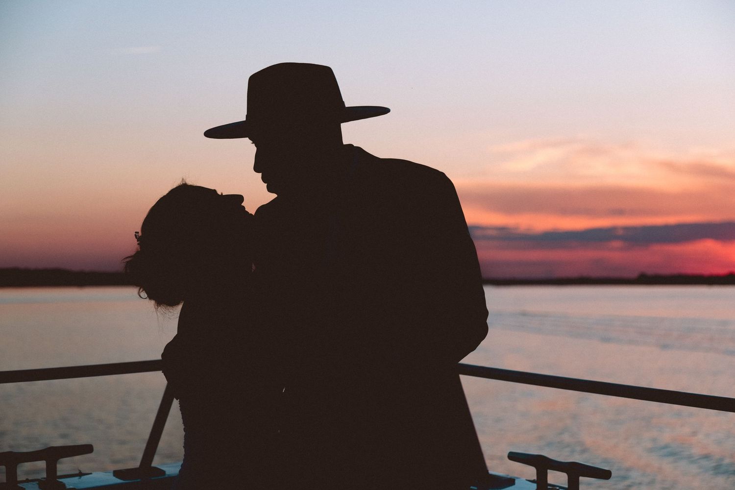 Silhouette of couple sharing a kiss on a boat deck against a stunning colorful sunset over water.