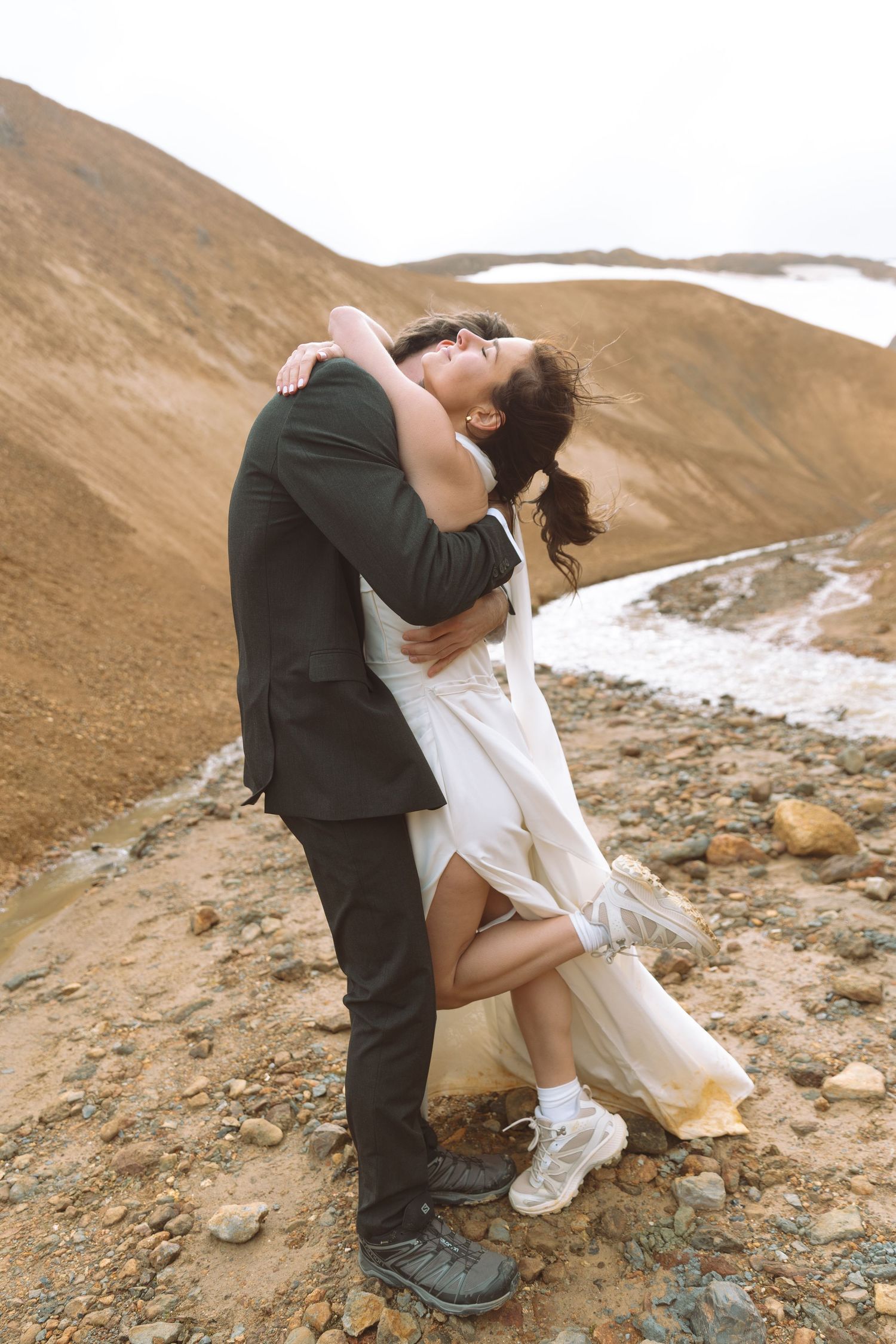 Bride wraps arms around groom's neck laughing joyfully during their outdoor mountain wedding in Iceland.