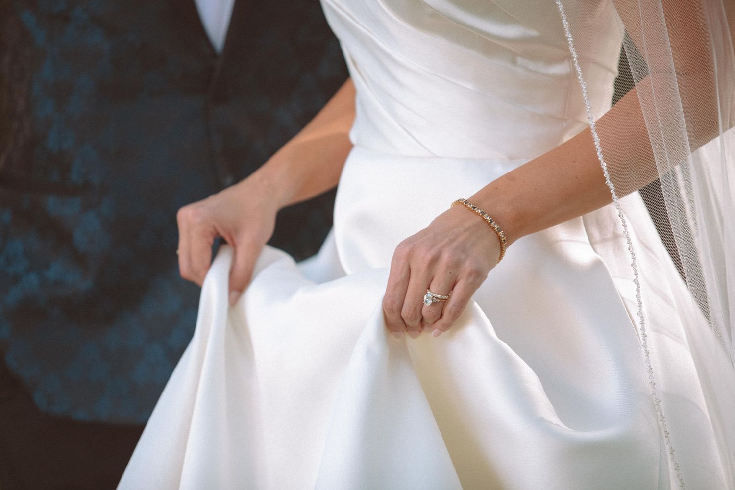 Close-up of bride holding wedding dress with diamond engagement ring and gold bracelet.