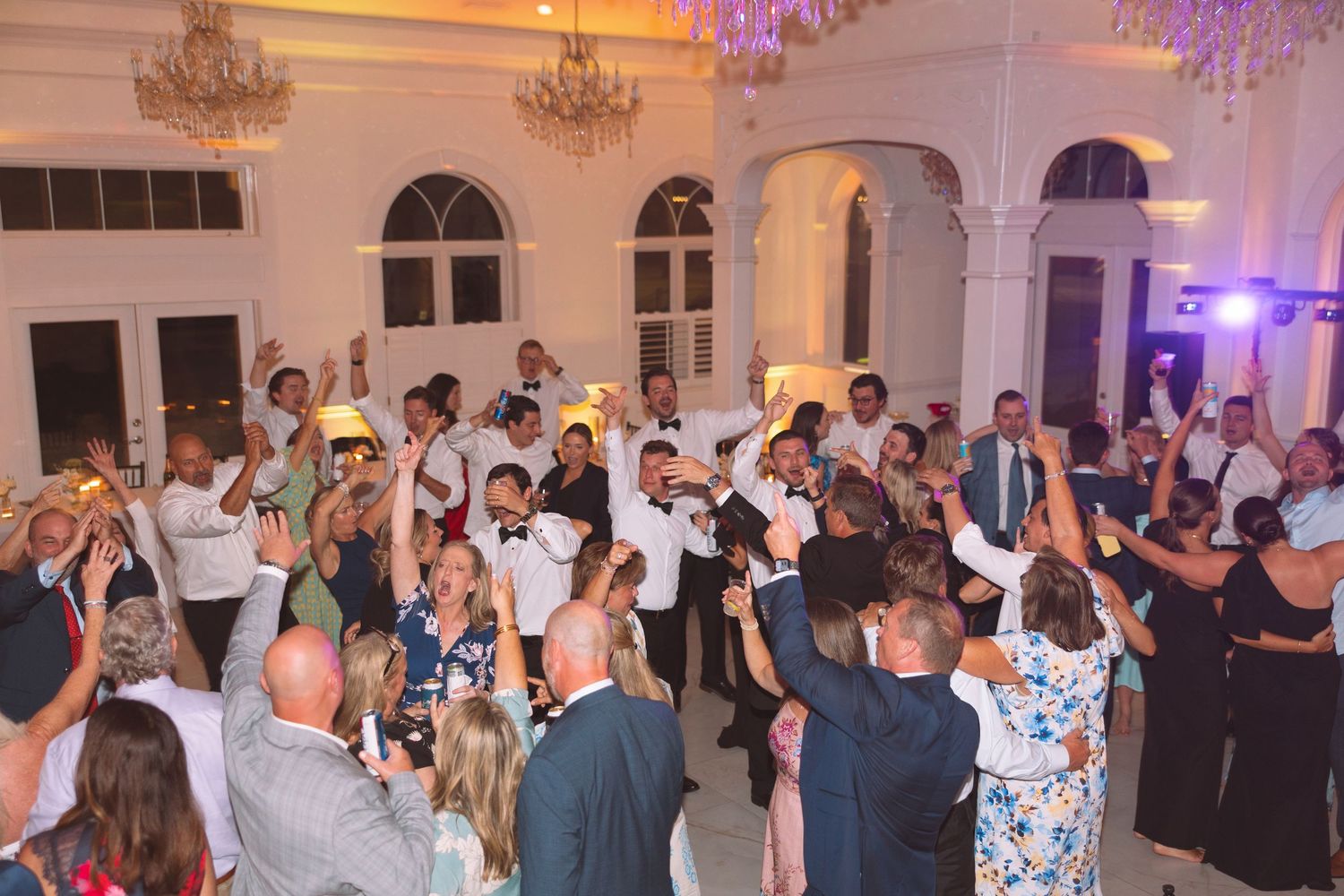 Elegant wedding reception with guests raising glasses in a grand ballroom with chandeliers.