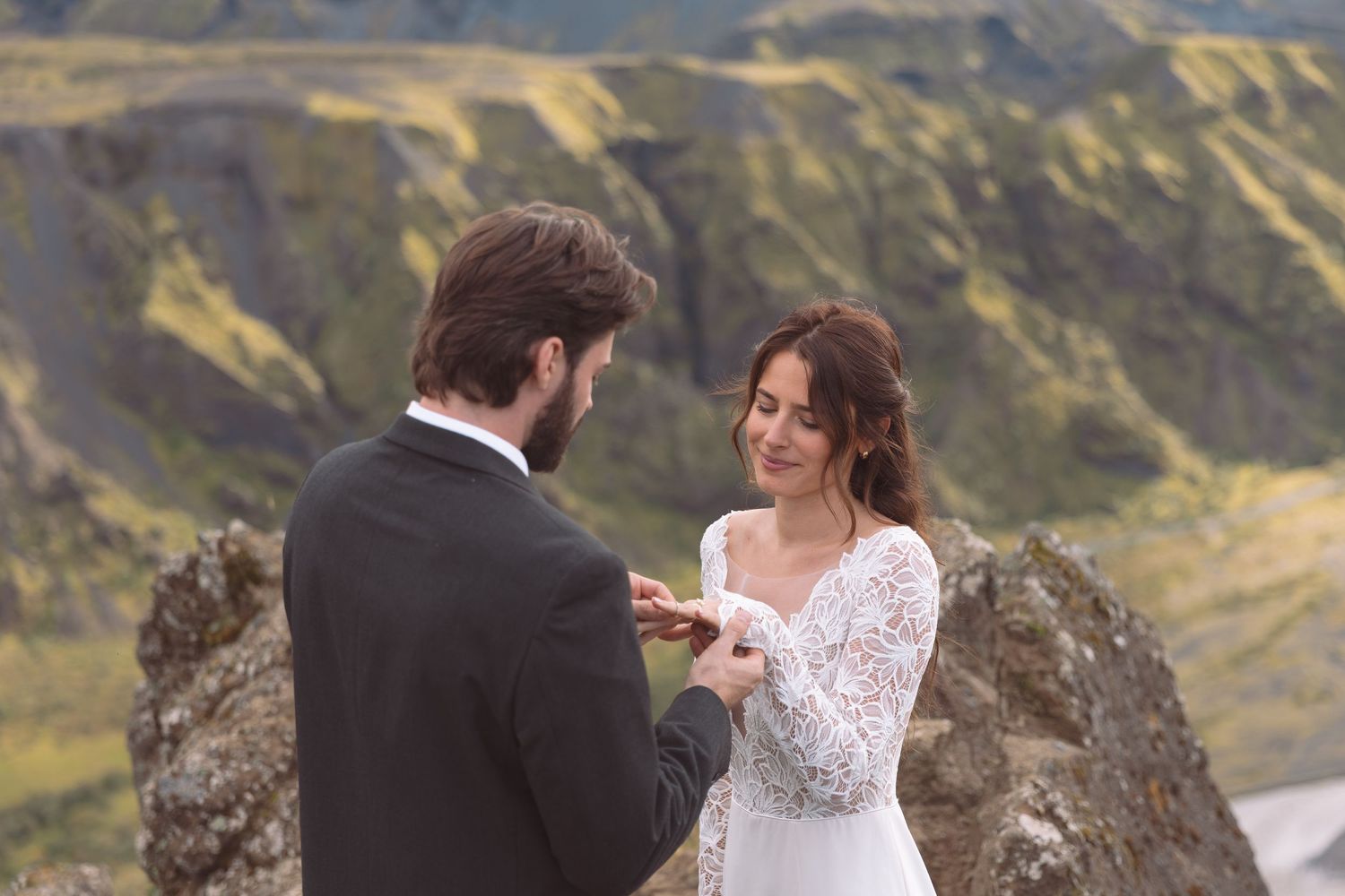 Groom places wedding ring on brides finger as she smiles during scenic Iceland mountain ceremony.
