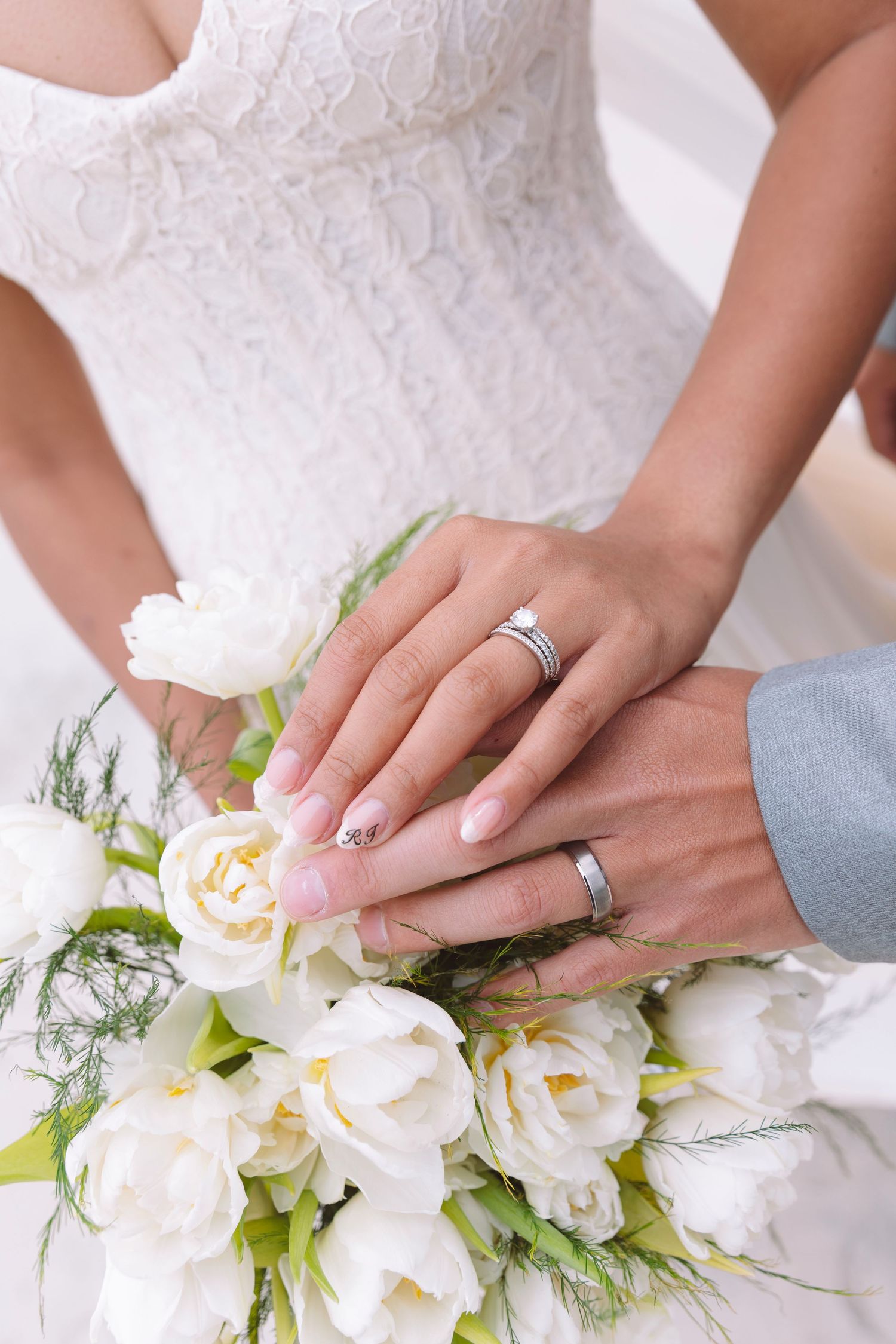 Newlyweds displaying wedding rings on hands resting over a bouquet of white tulips.