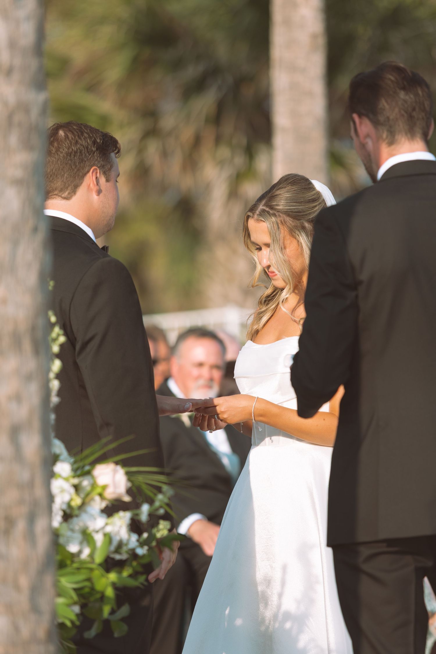 Bride reading vows to groom during an outdoor wedding ceremony surrounded by palm trees.