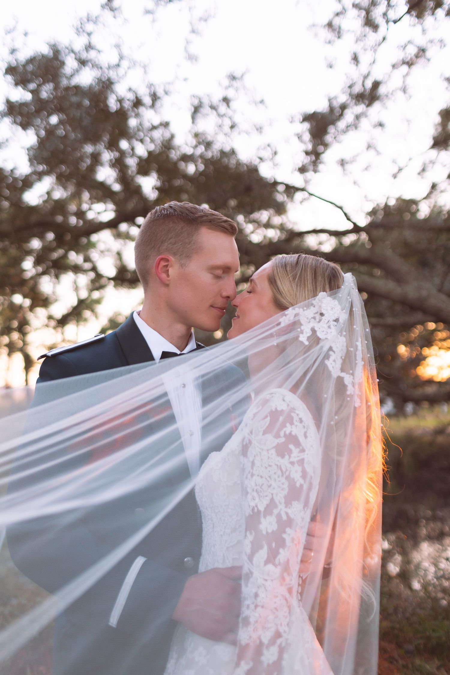 Bride and groom sharing a romantic kiss under flowing lace veil outdoors.