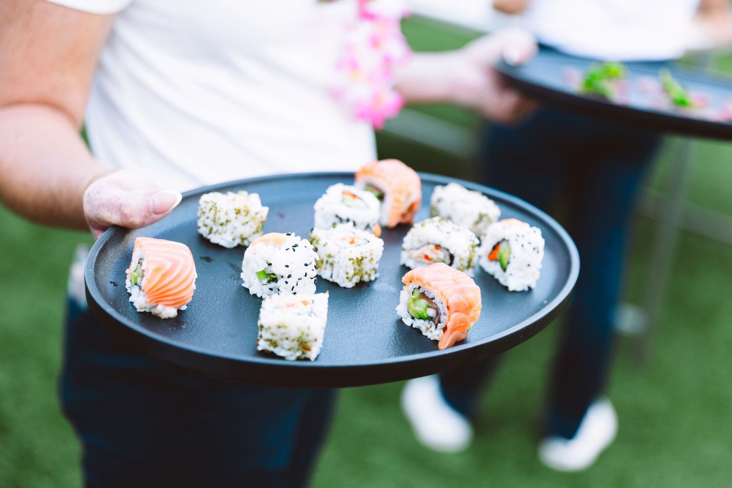 Catered sushi platter with salmon nigiri and maki rolls served on a black tray at an outdoor event.