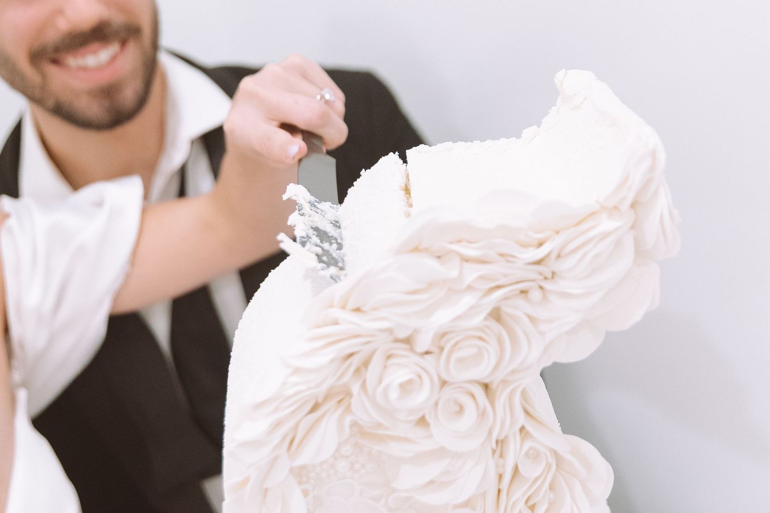 A baker decorates an elegant white wedding cake adorned with fondant roses using a spatula.